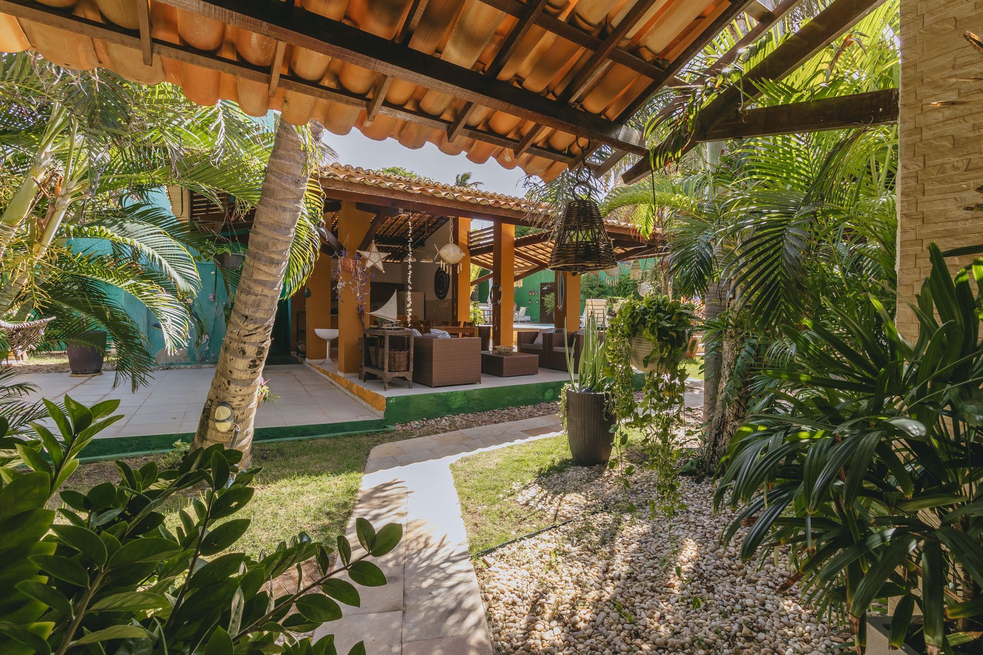 Área de estar tropical ao ar livre com vegetação exuberante, caminho e assentos na sombra.