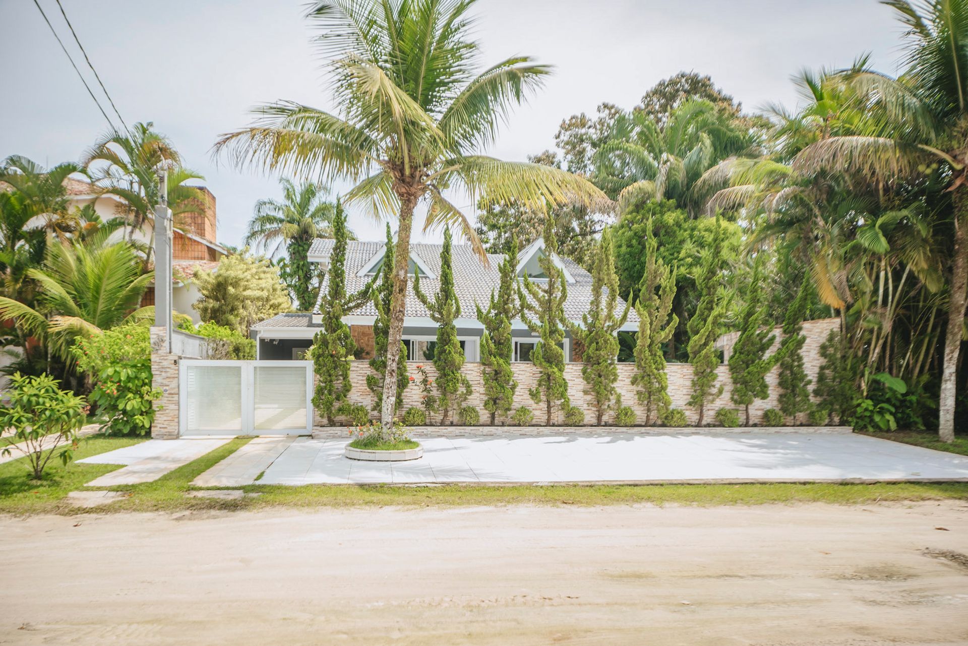 Casa de praia com cerca branca, telhado cinza claro e árvores verdejantes.