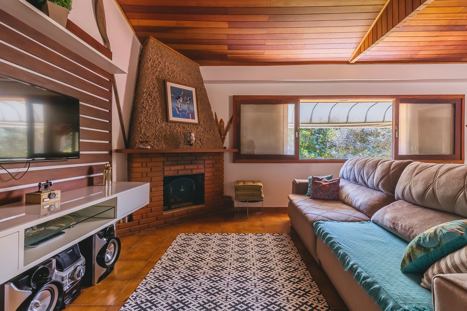 Sala de estar aconchegante com lareira, TV e sofá perto de uma janela com luz natural.