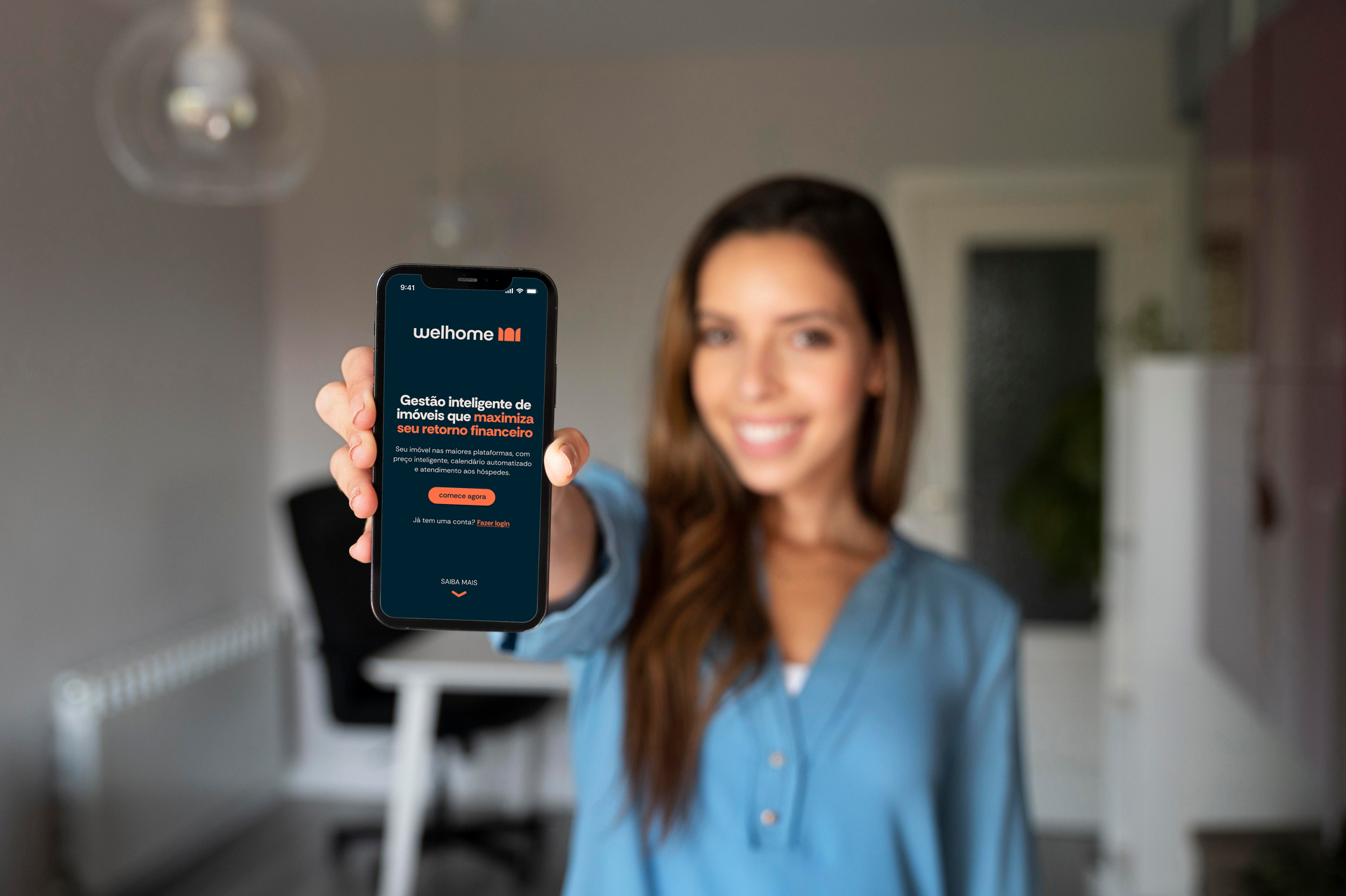 Mulher sorridente, segurando um celular com a tela de um aplicativo, oferecendo o aparelho em direção à câmera.