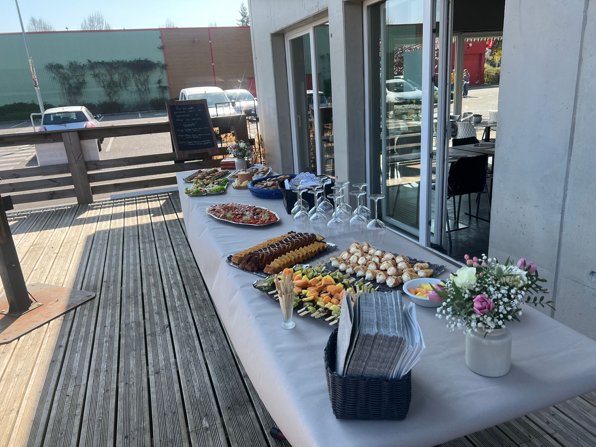 Buffet sur une terrasse avec divers mets, verres et fleurs.