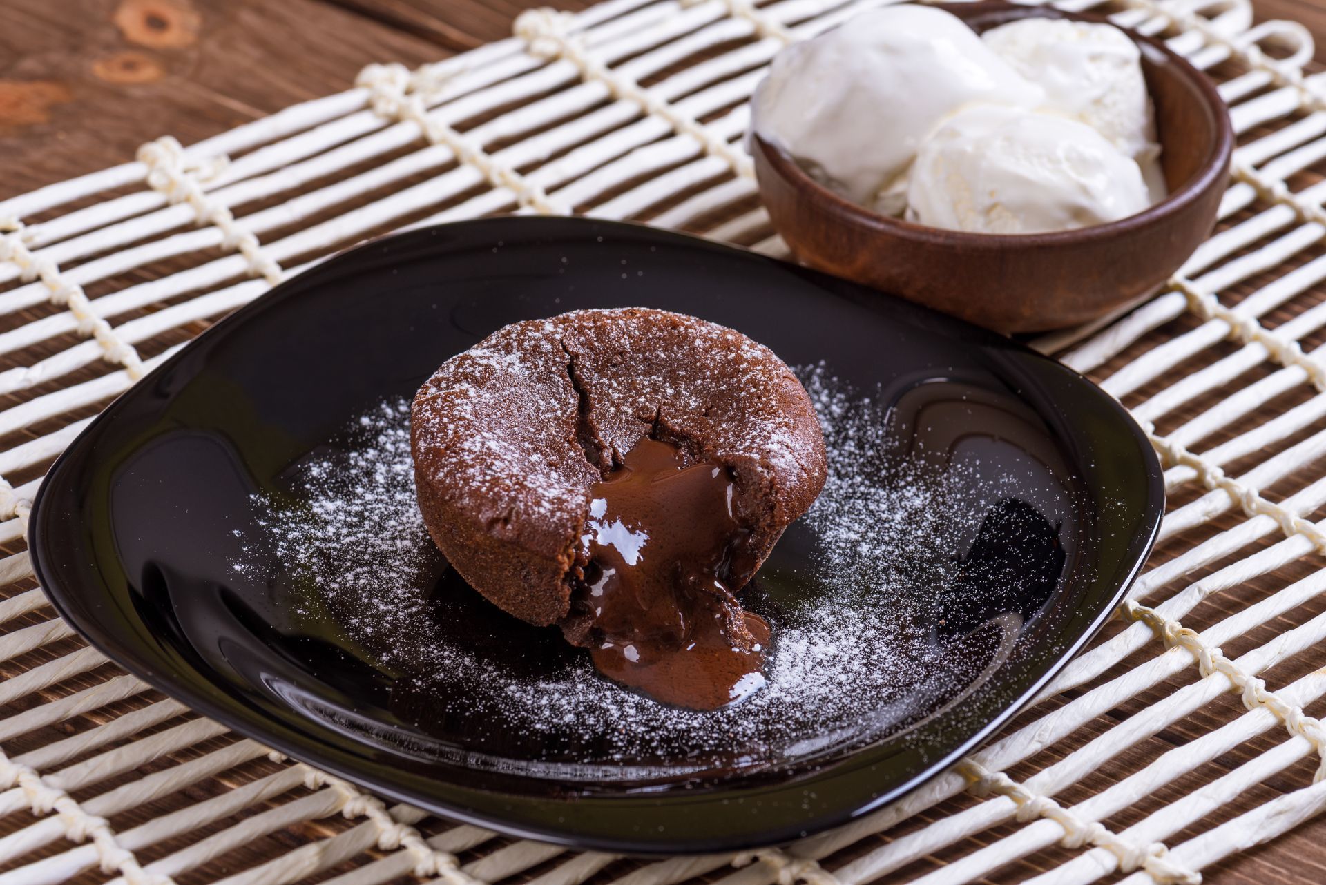 Gâteau au chocolat fondant dans une assiette noire, saupoudré de sucre glace et accompagné de glace à la vanille.