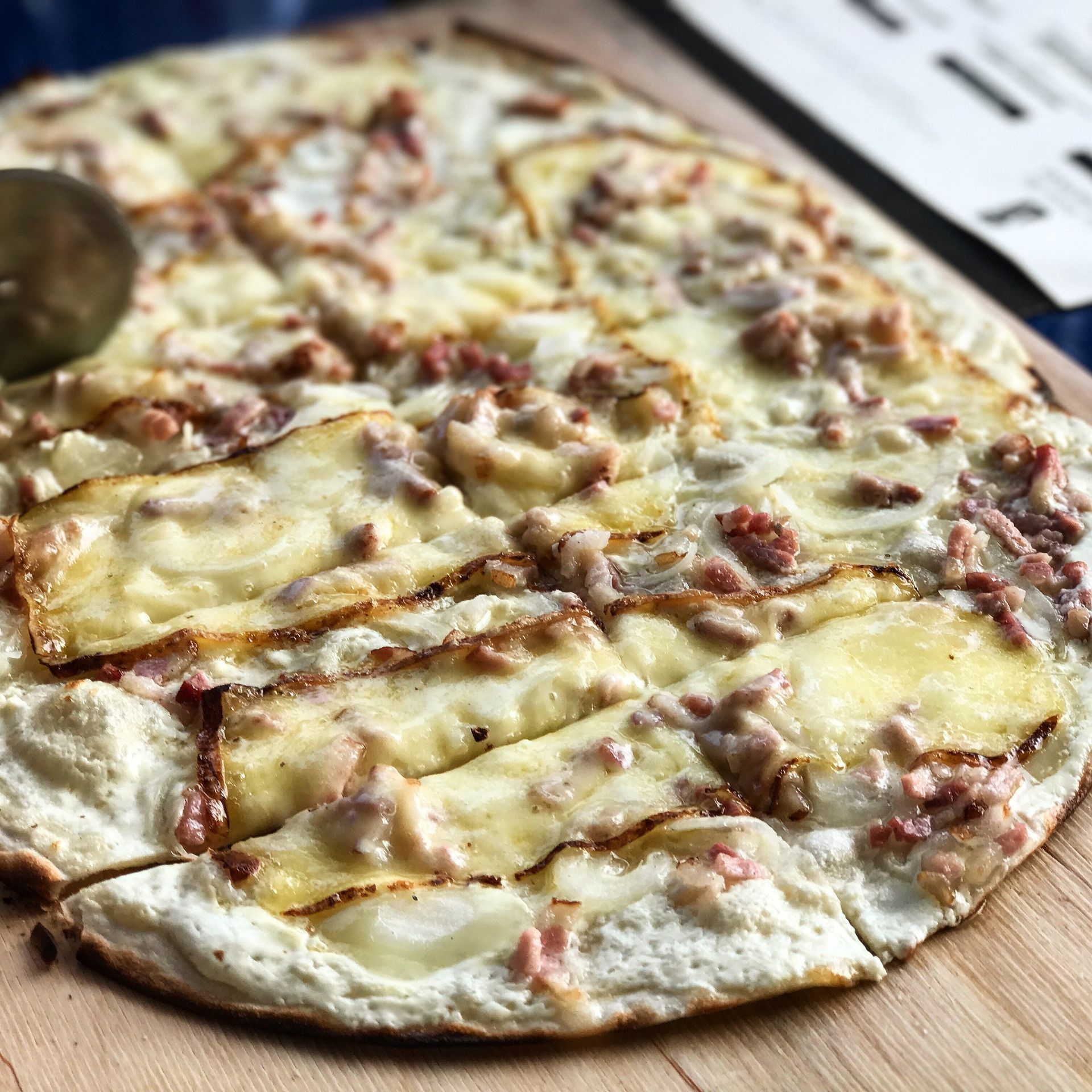 Flammeküche aux oignons, au bacon et au fromage, coupée sur une planche en bois.