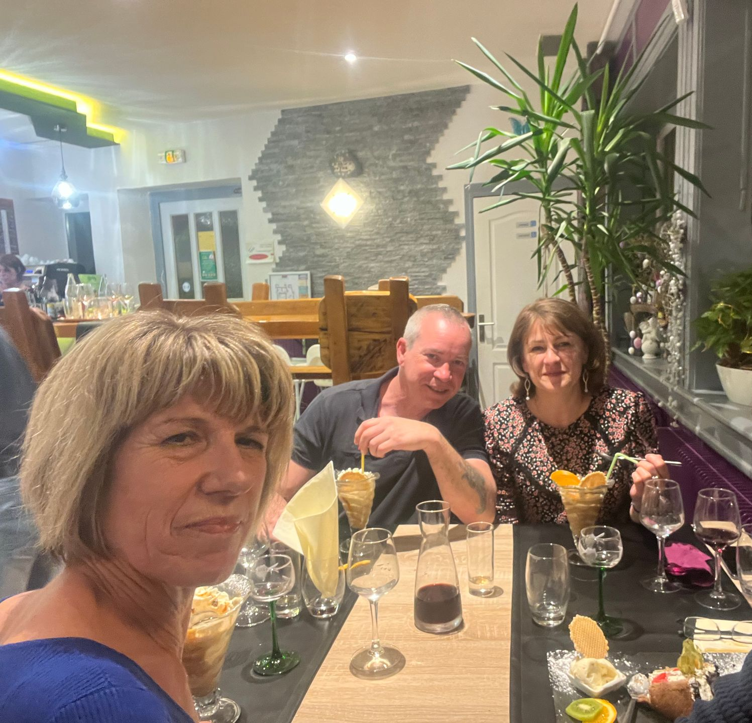 Trois personnes dégustent un dessert au restaurant. Une femme au premier plan, deux personnes en arrière-plan.