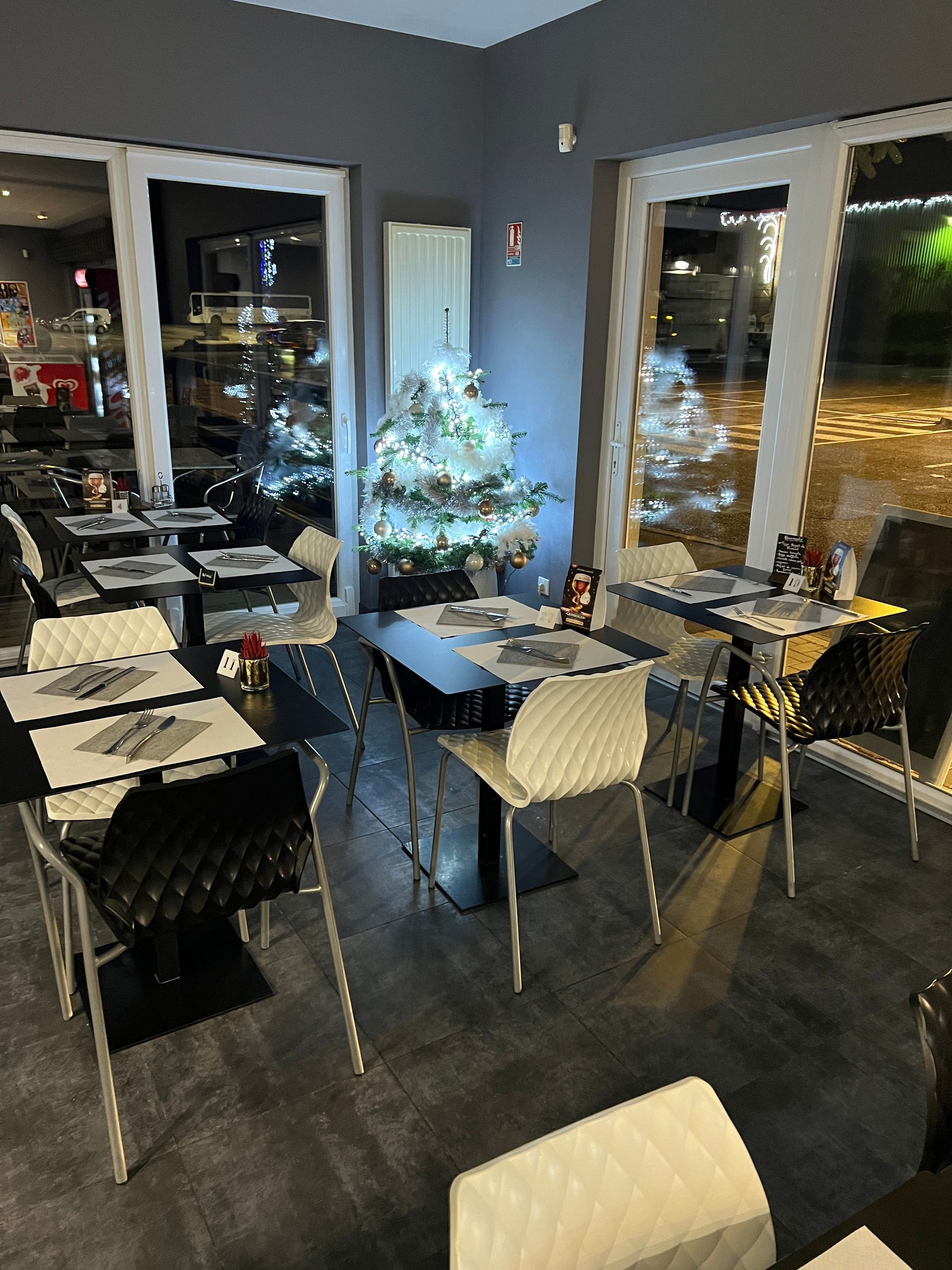 Intérieur d'un restaurant avec des tables, des chaises et un sapin de Noël près de la fenêtre.