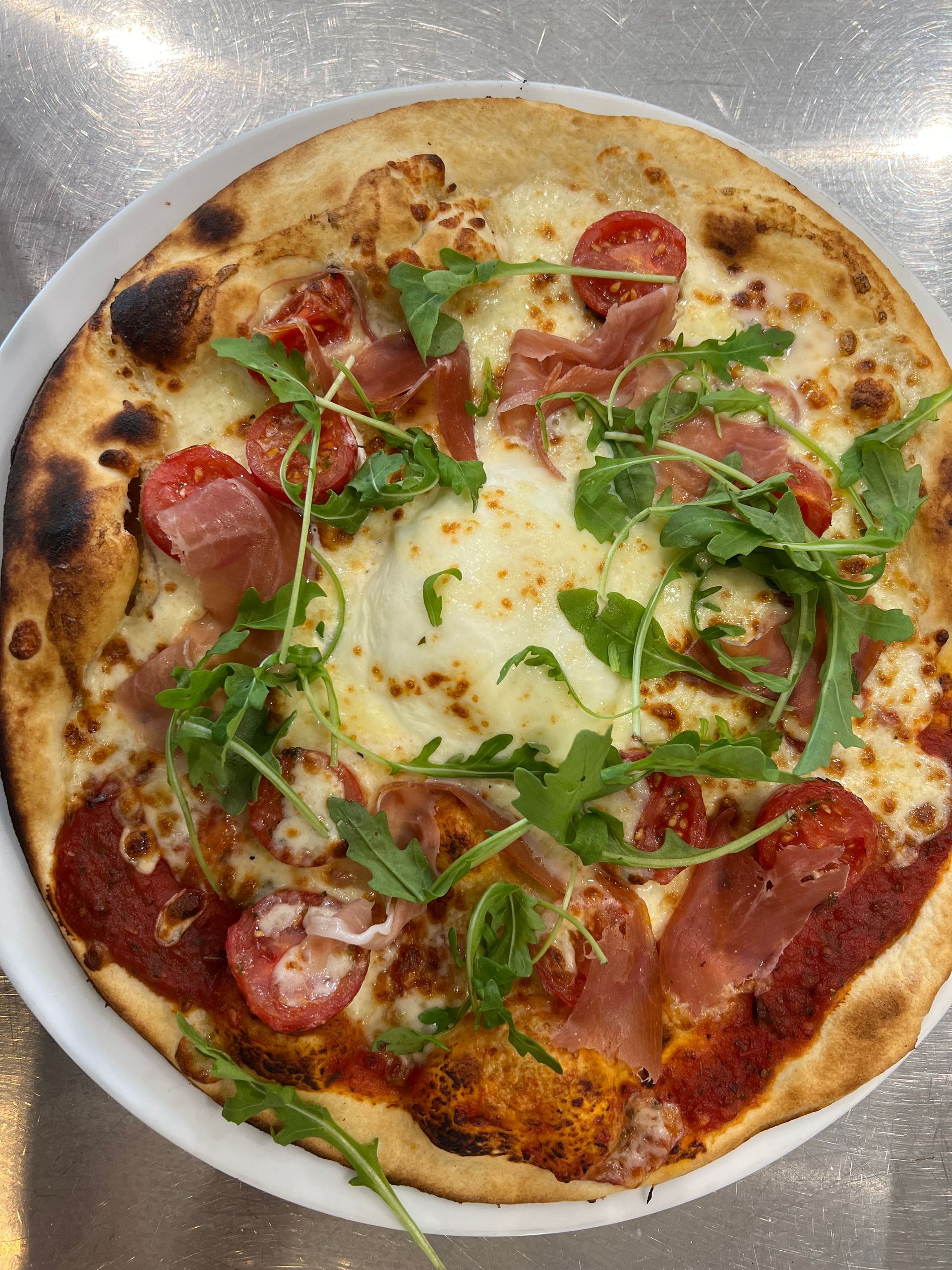 Pizza au prosciutto, à la roquette et aux tomates dans une assiette blanche.