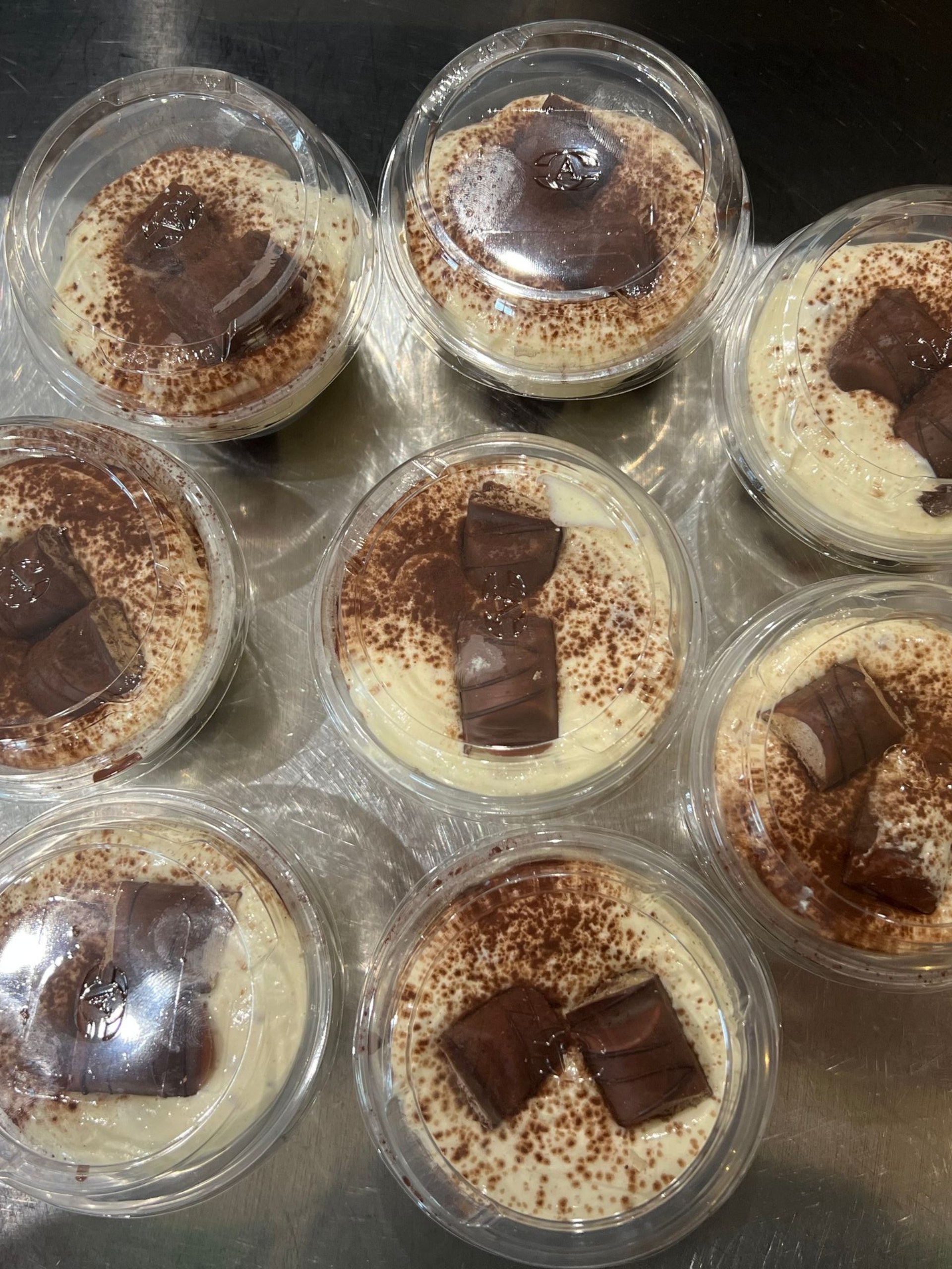 Desserts présentés dans des récipients transparents, nappés de chocolat et de cacao en poudre, disposés sur une surface.