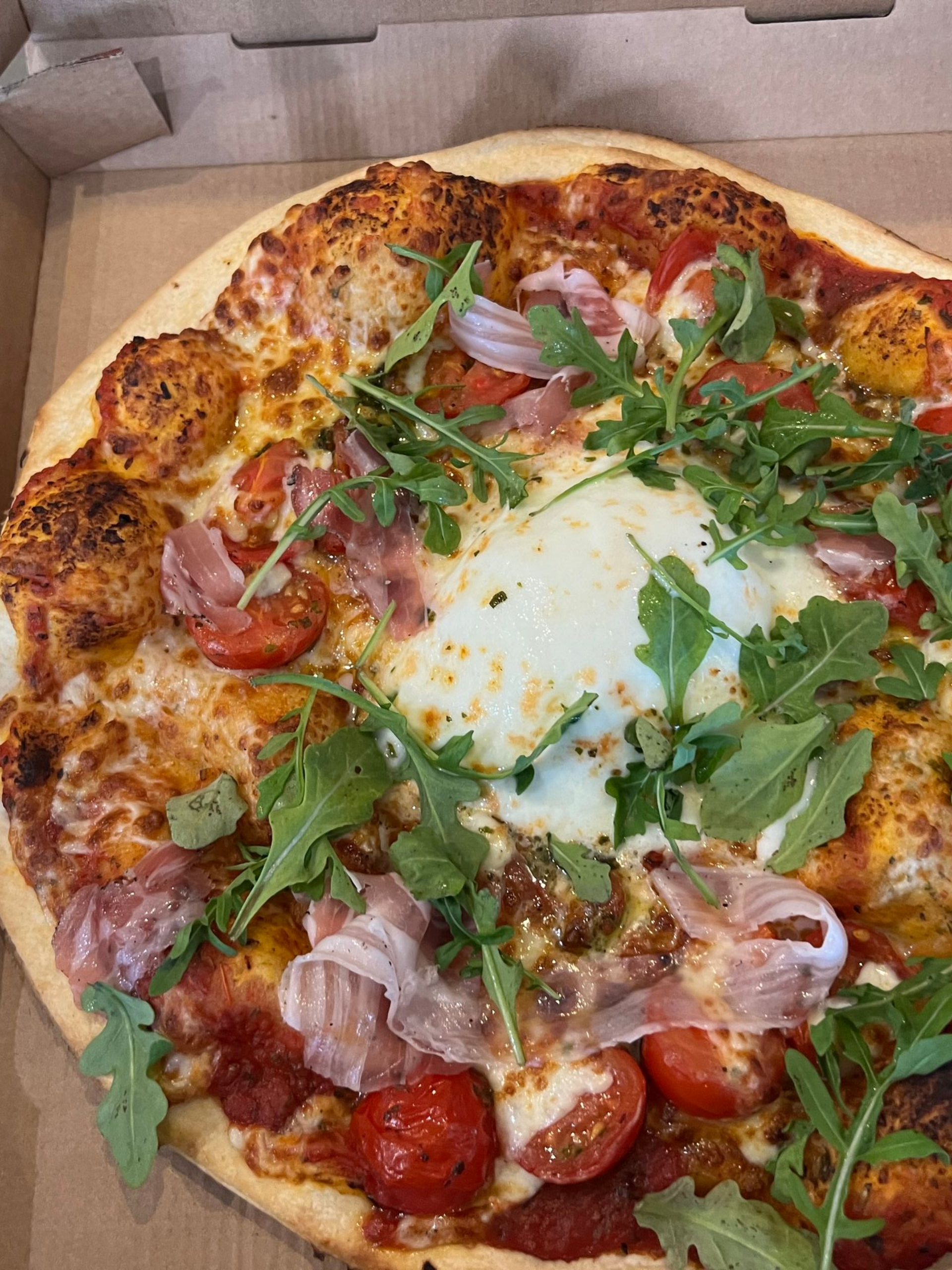 Pizza avec roquette, prosciutto, tomates et une généreuse quenelle de mozzarella.