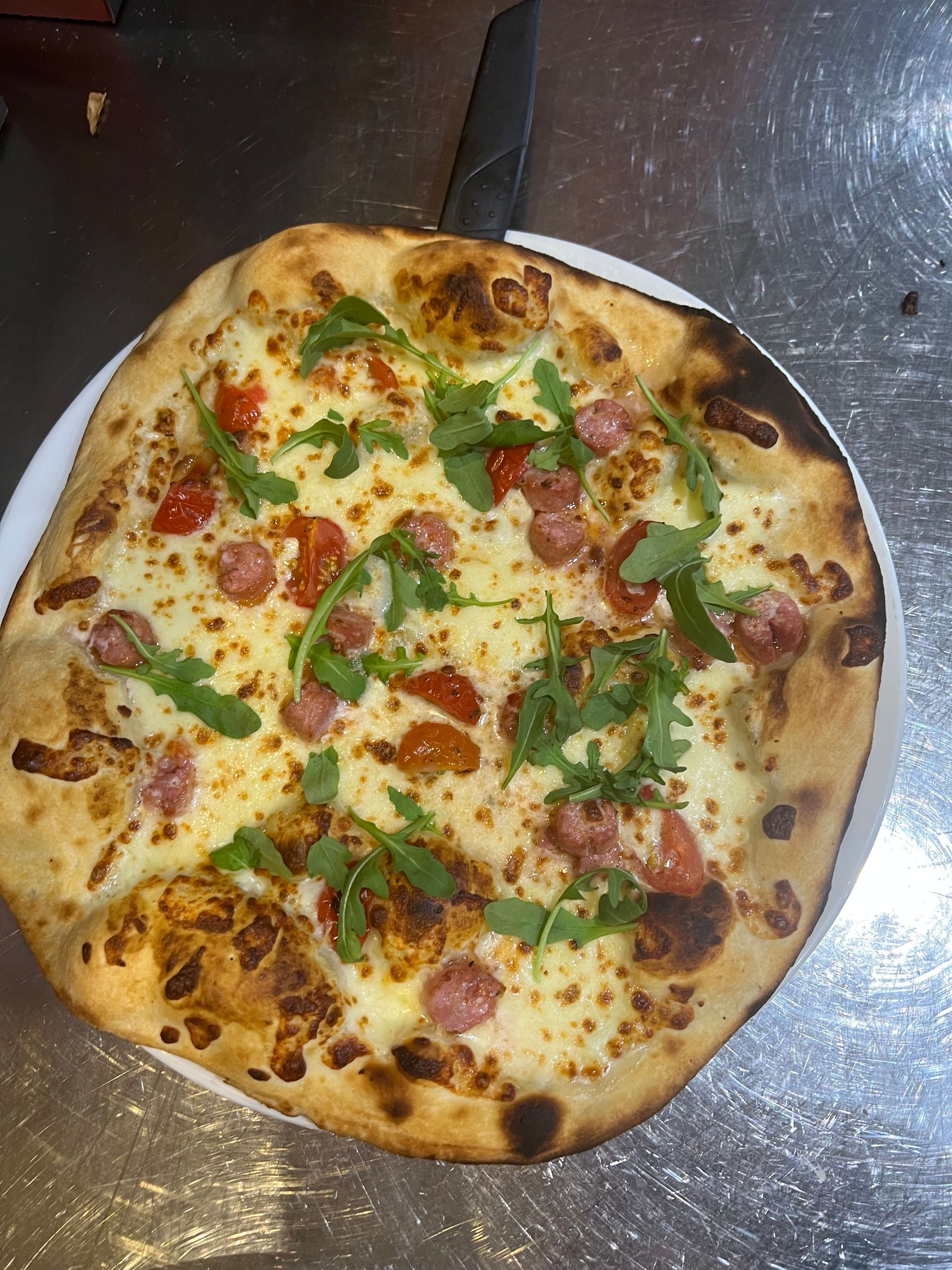 Pizza avec fromage, tomates, saucisse et roquette dans une assiette blanche.