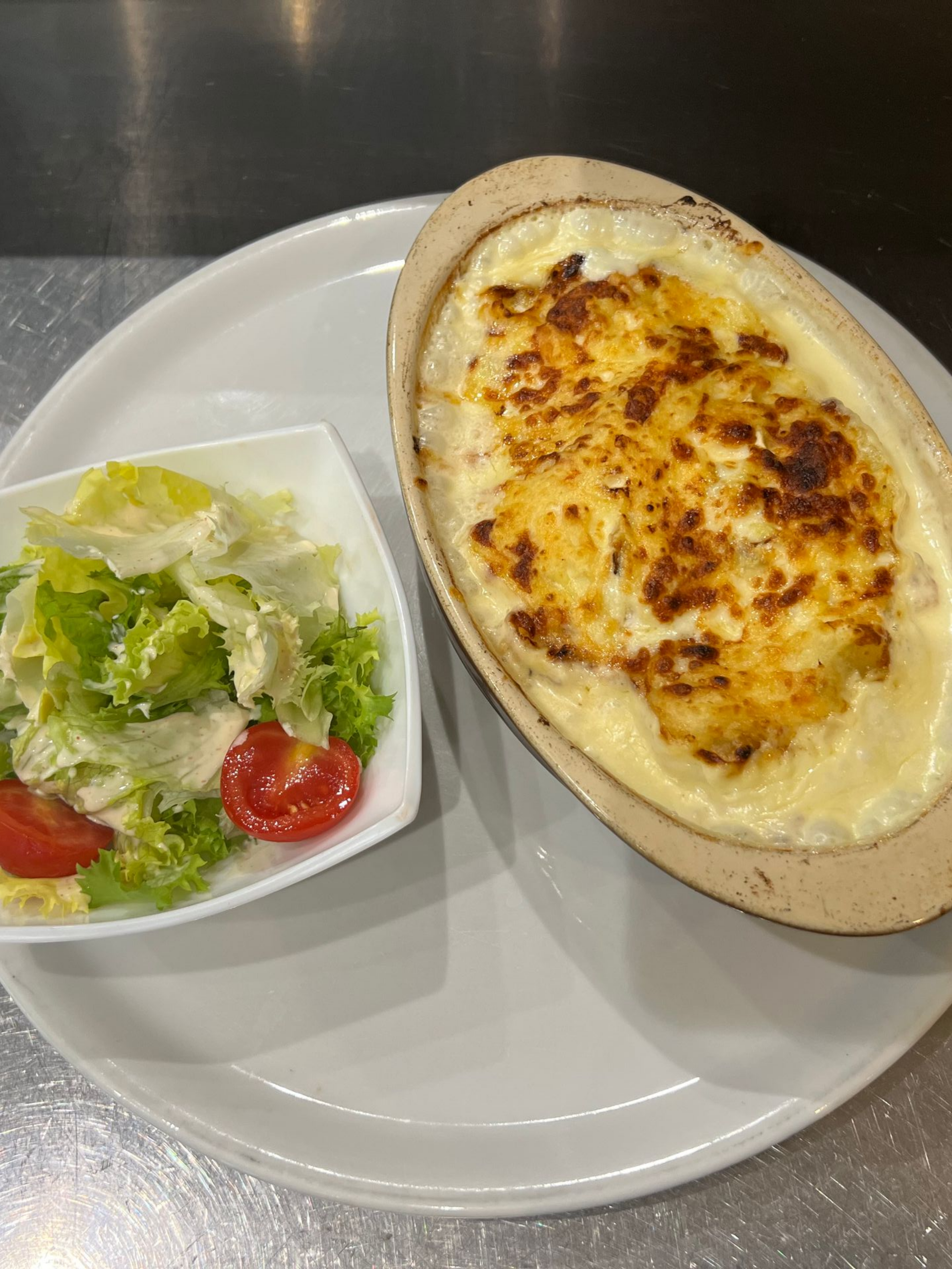 Plat cuit au four avec une surface dorée, accompagné d'une salade dans une assiette blanche.