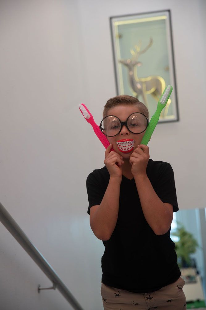 Kind mit großer Brille und zwei großen Zahnbürsten