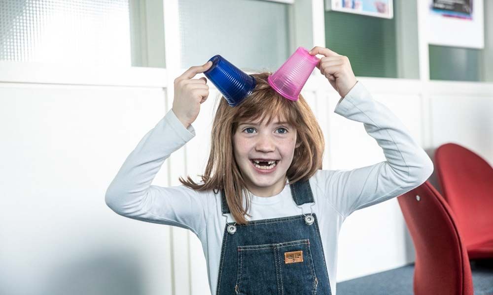 Kind setzt sich zwei Becher auf den Kopf