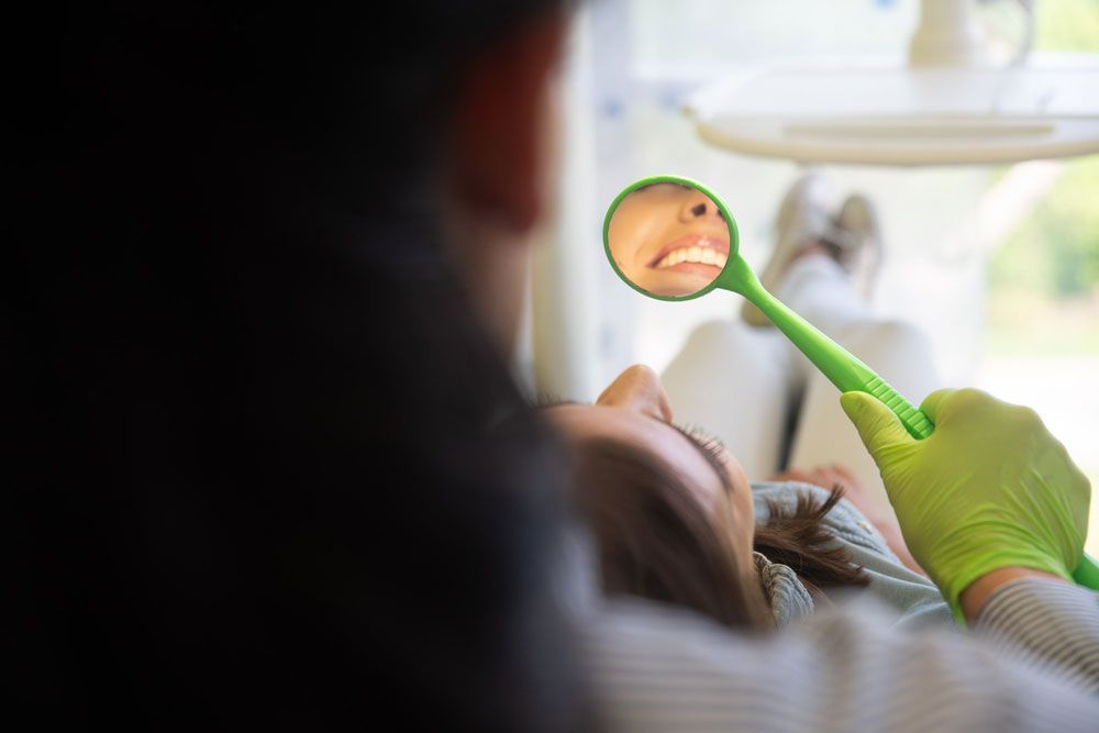 Frau betrachtet Zähne in einem kleinen Spiegel