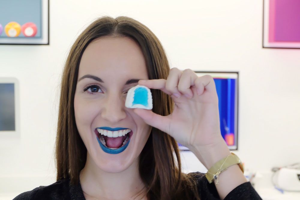 Frau mit blau geschminkten Lippen hält ein Gebissmodell vor dem Auge