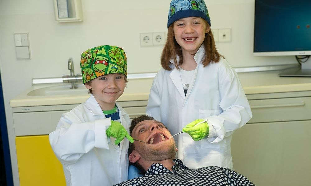 Zwei Kinder mit Zahnarztinstrumenten behandeln einen Erwachsenen