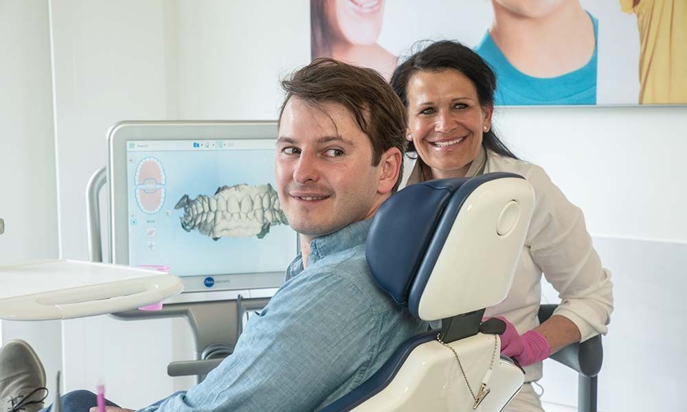 Lächelnder Patient und Zahnärztin vor einem Gebissbild