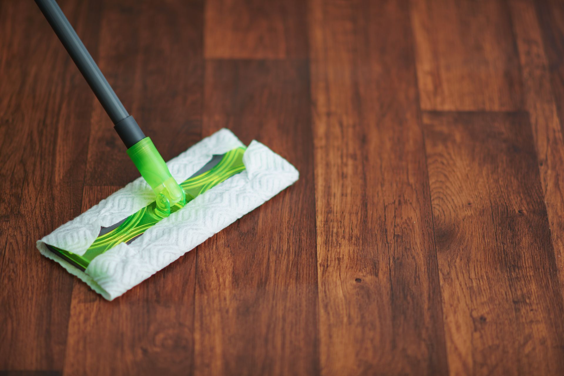 Mit einem Mopp wird ein Holzboden gereinigt.
