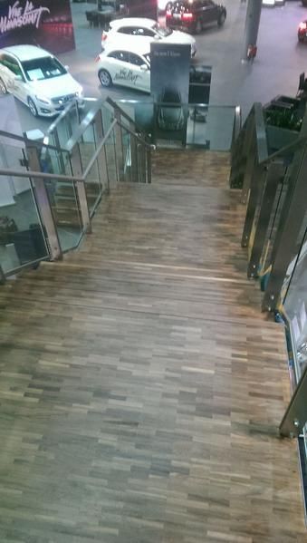 Eine Treppe mit Holzboden und Glasgeländer führt zu einem Autohaus.