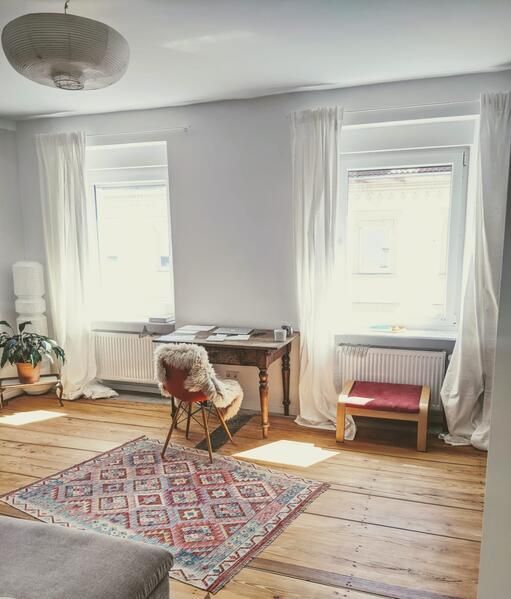 Ein Wohnzimmer mit Teppich, Stuhl, Schreibtisch und Fenstern.