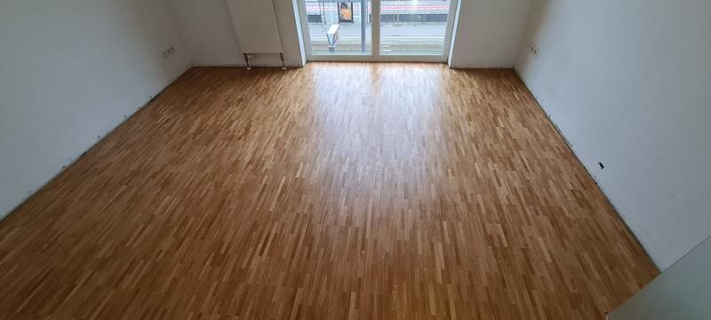 Ein leerer Raum mit Holzboden und einer Glasschiebetür.