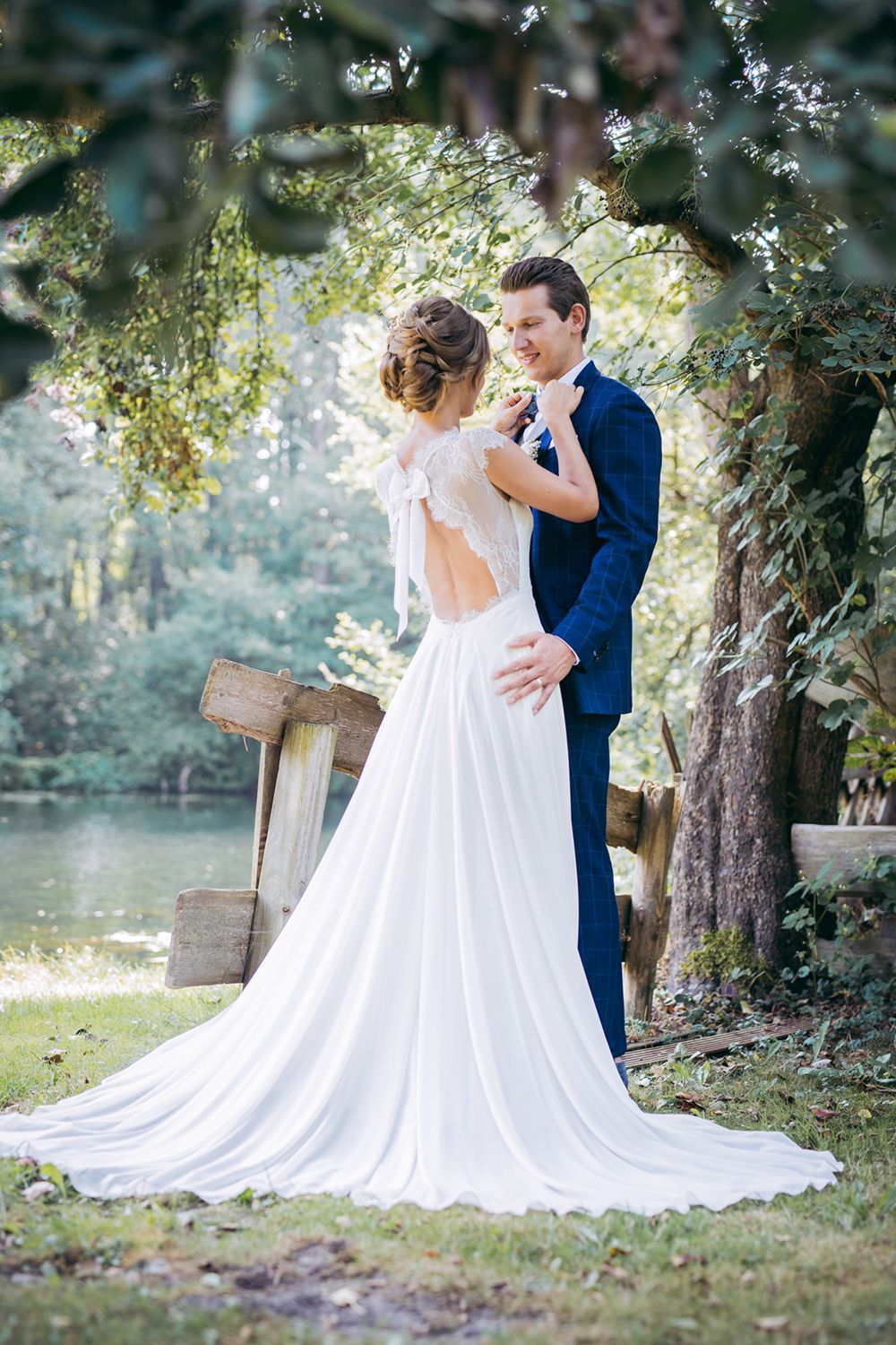 Braut und Bräutigam in einem Wald an einem See, Braut im weißen Kleid, Bräutigam im blauen Anzug, sie schauen sich an.