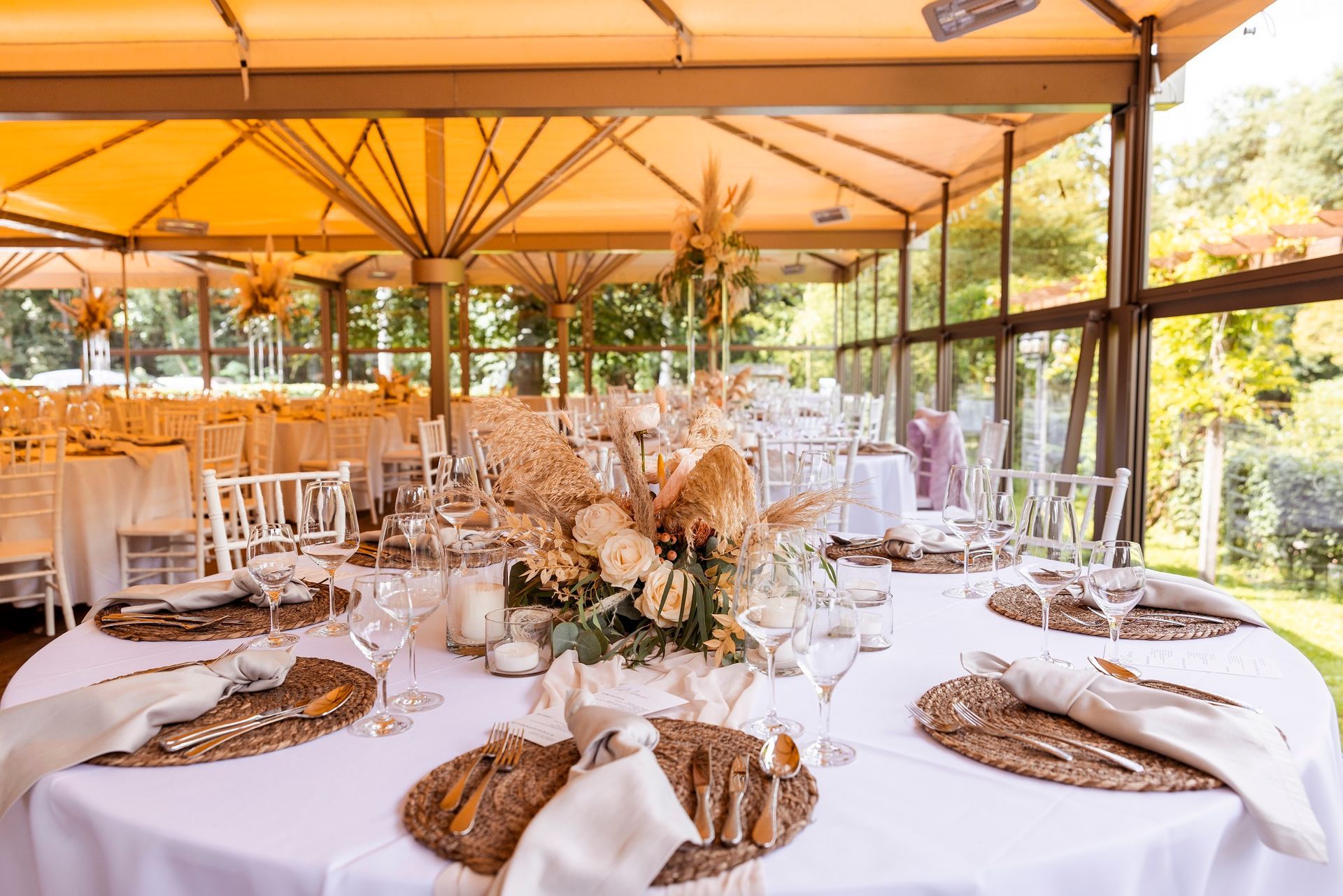 Runde Tische für eine Veranstaltung im Freien, mit Blumengestecken unter einem Baldachin.