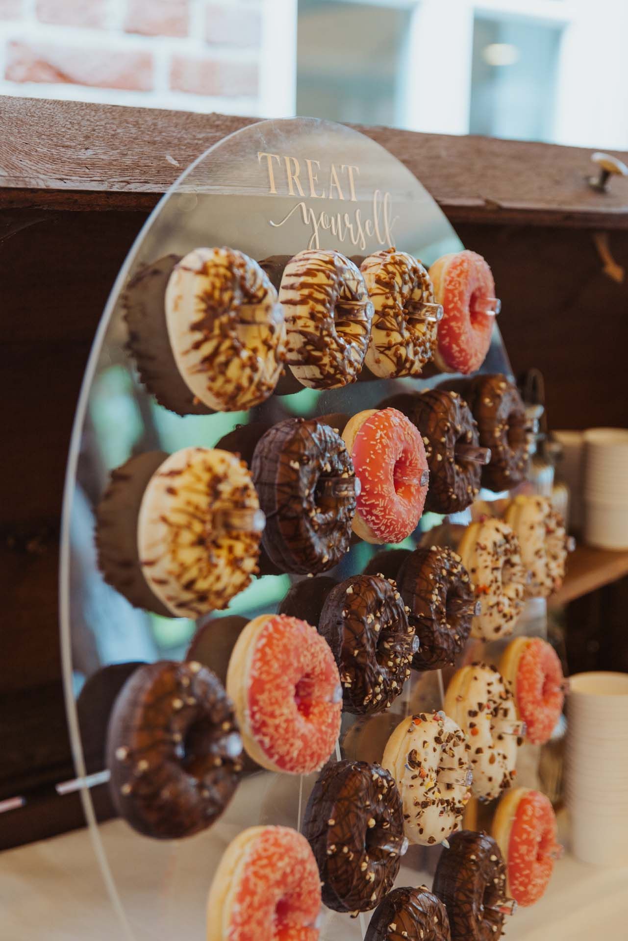 Donut-Ausstellung mit glasierten Donuts in verschiedenen Geschmacksrichtungen vor einer durchsichtigen Acryltafel mit der Aufschrift „Gönnen Sie sich etwas.“