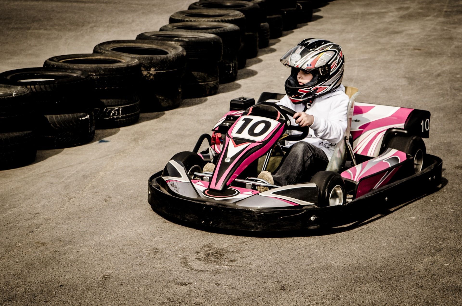 Junge Person in einem rosa-schwarzen Go-Kart, mit Helm, auf einer Strecke neben Reifenstapeln.