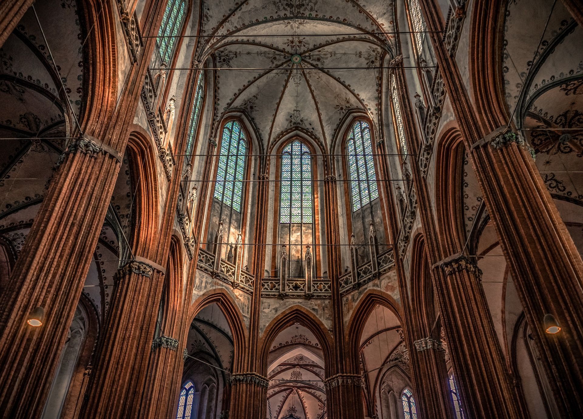 Innenansicht einer gotischen Kathedrale mit hohen Bogenfenstern und verzierten Ziegelsäulen.