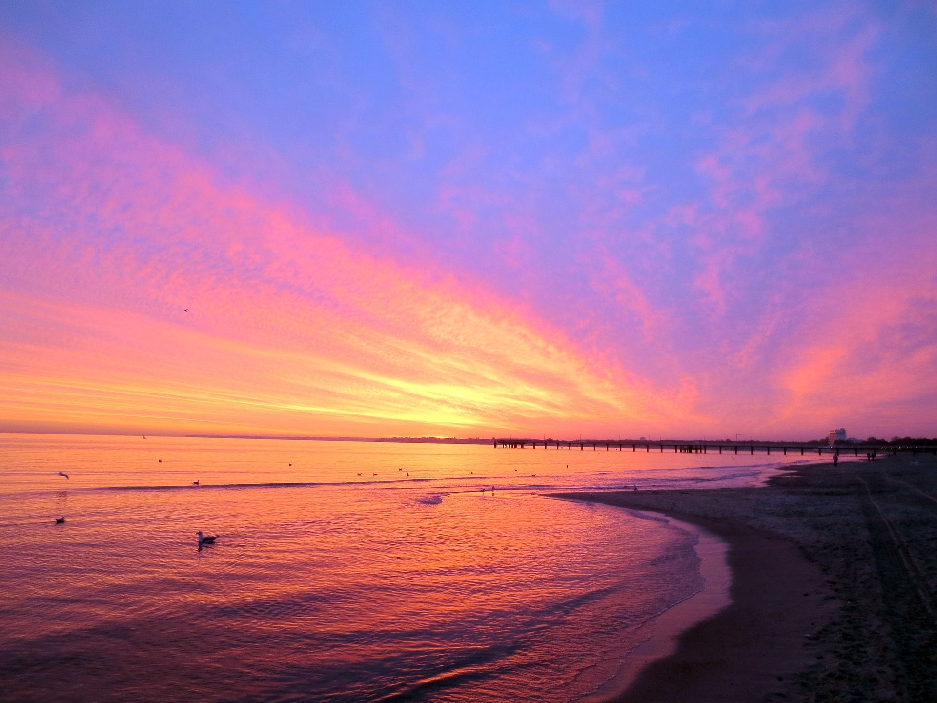 Strahlender Sonnenuntergang über dem Meer, mit Rosa-, Orange- und Lilatönen, die sich im Wasser spiegeln.