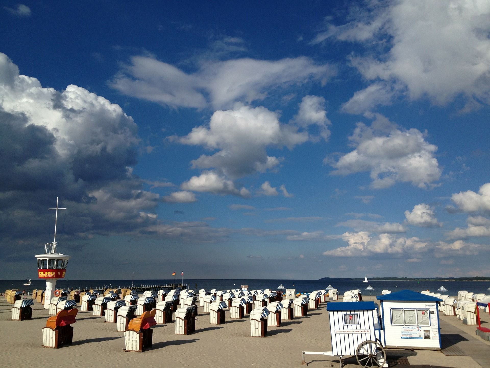 Strandszene mit vielen Strandkörben unter einem teilweise bewölkten blauen Himmel; ein Rettungsschwimmerturm ist sichtbar.