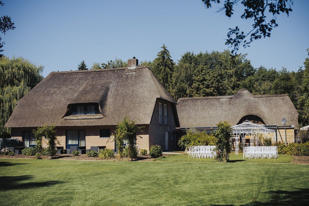Ein strohgedecktes Holzgebäude mit gepflegtem Rasen und Bäumen unter blauem Himmel.