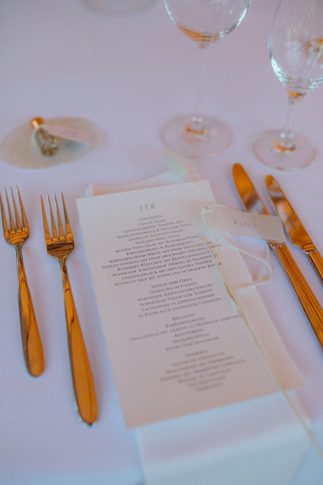 Formelles Tischgedeck mit goldenem Besteck, Speisekarte und Weingläsern. Weiße Tischdecke.