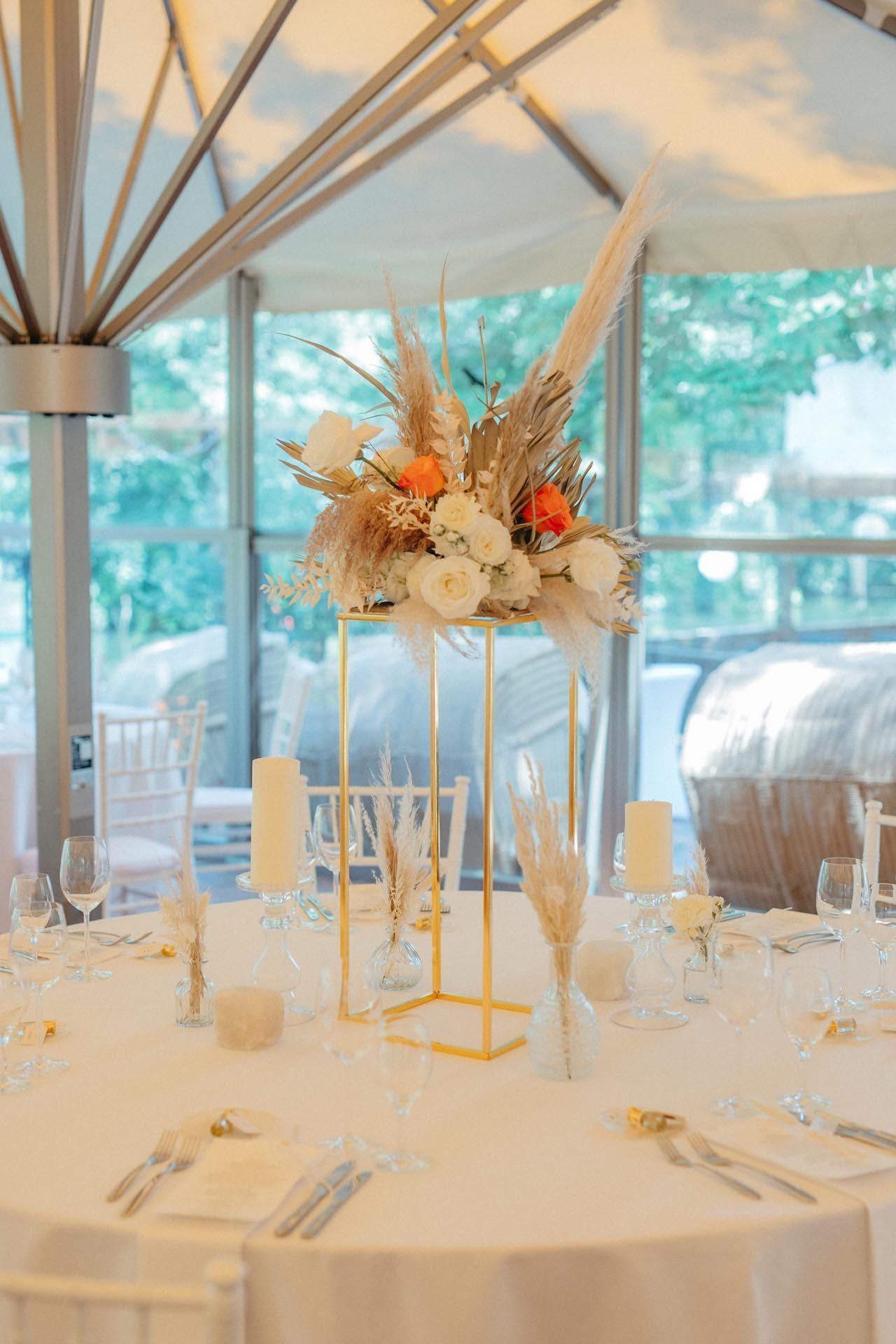 Goldenes Blumengesteck auf einem für eine Hochzeit gedeckten Tisch. Weiße Tischdecke, Kerzen und Glaswaren.