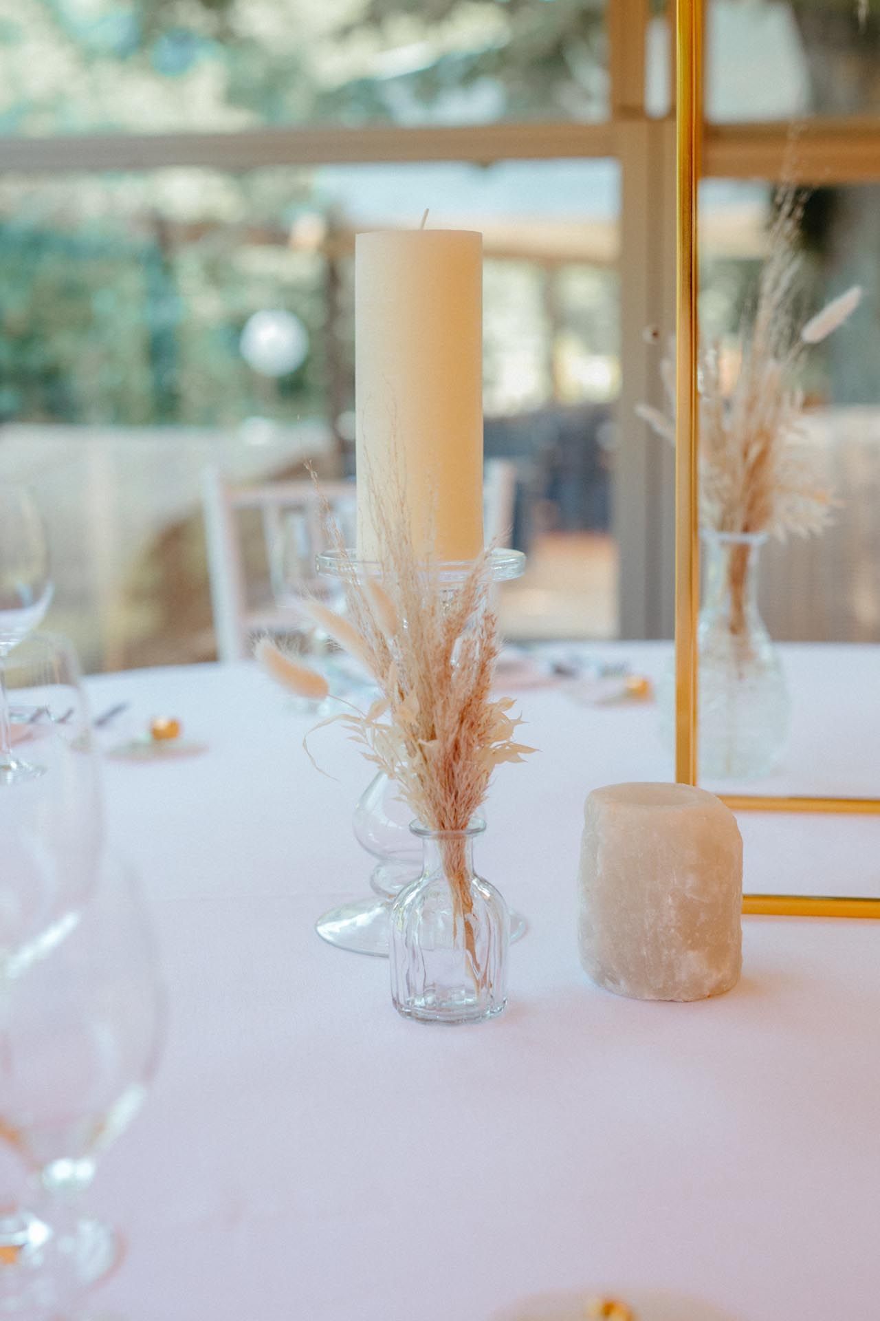 Elegante Tischdekoration mit einer hohen Kerze, Trockenblumen und Glasvasen.