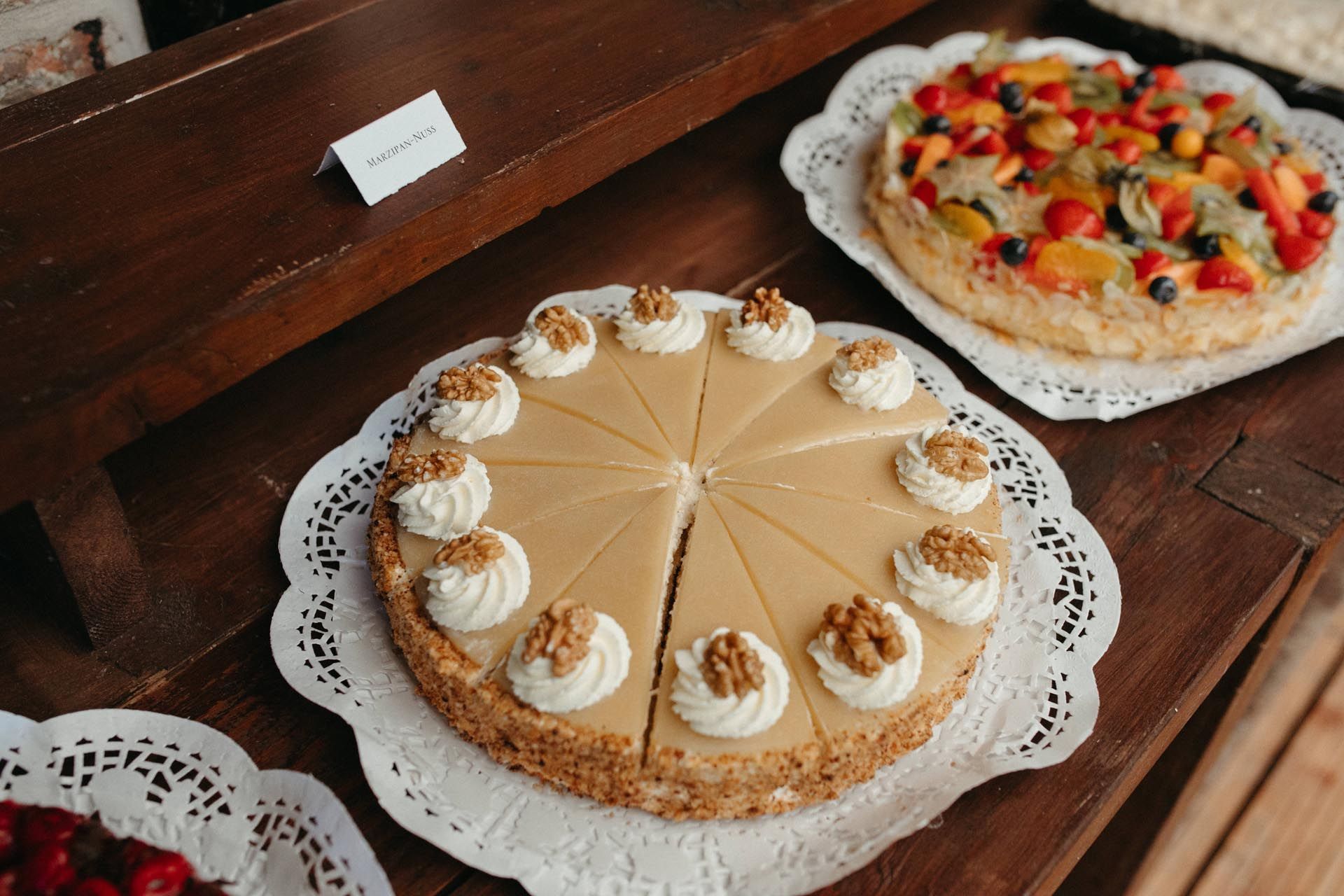 Ausgestellte Kuchen, darunter ein Karamellkuchen mit Walnüssen und eine Obsttorte auf einer Holzoberfläche.