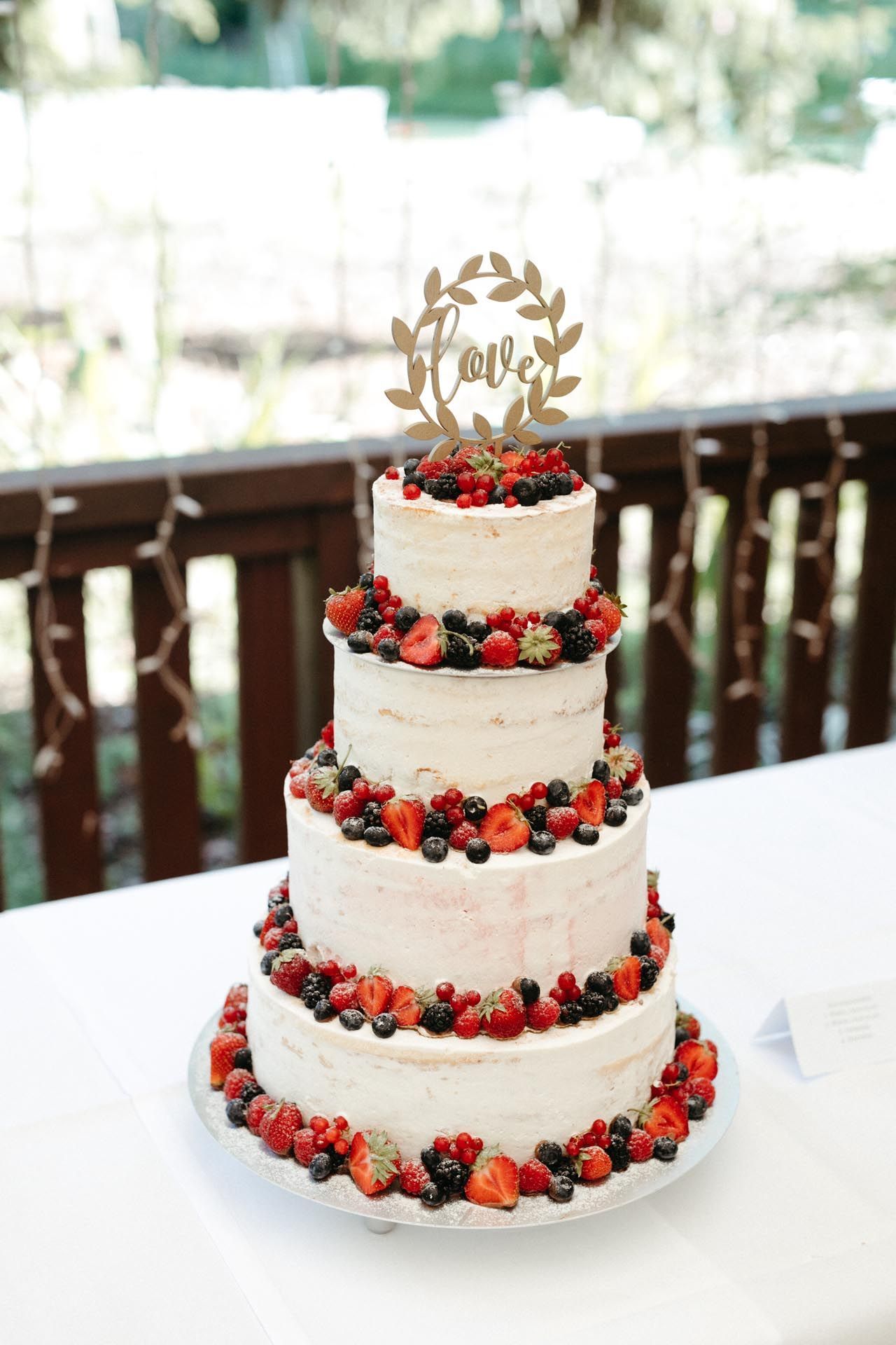 Vierstöckige Hochzeitstorte, Beeren zwischen den Schichten, garniert mit „Liebe“ und einem Blattmuster.