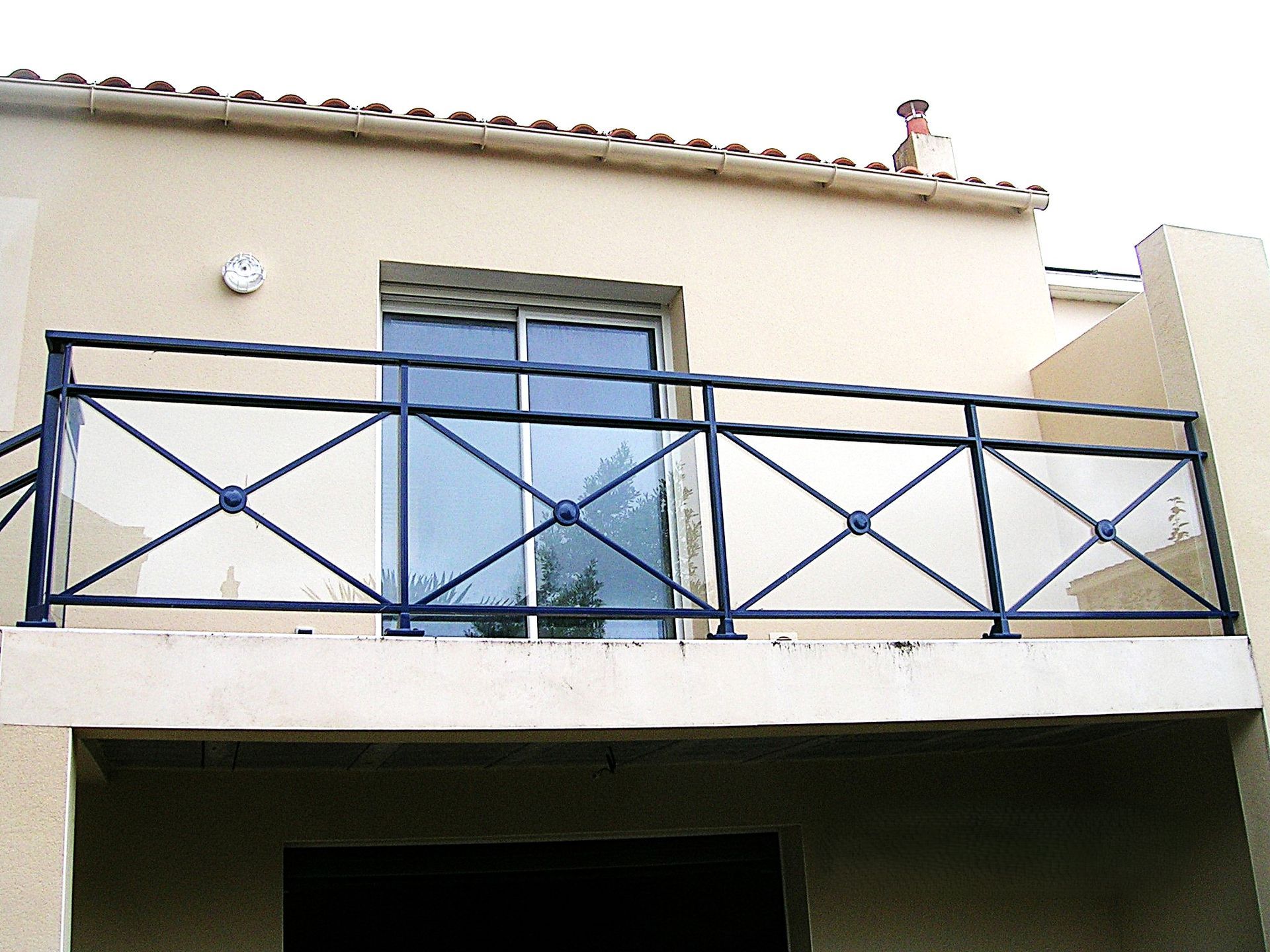 Rambarde de balcon bleue sur un immeuble couleur crème avec une fenêtre et une petite statue sur le toit