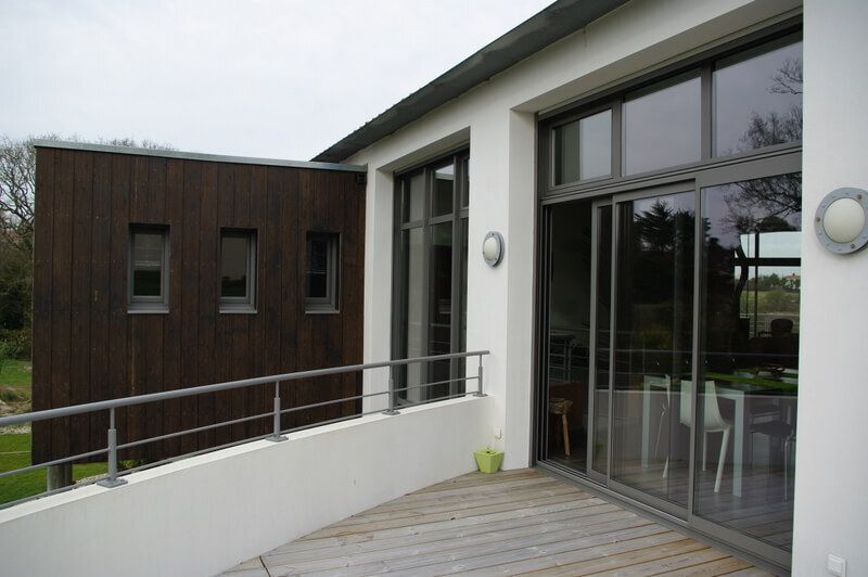 Entrée de maison moderne avec portes vitrées, rampe blanche et terrasse en bois