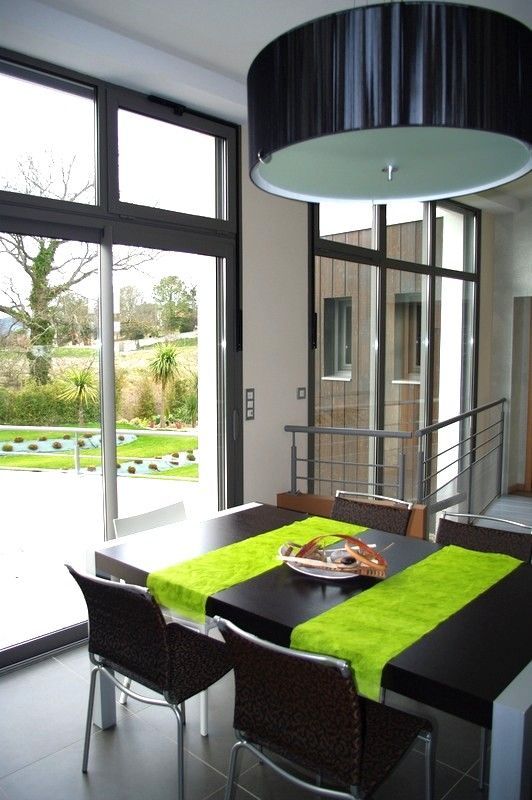 Salle à manger moderne avec table noire, chemin de table vert vif et grandes fenêtres donnant sur un jardin