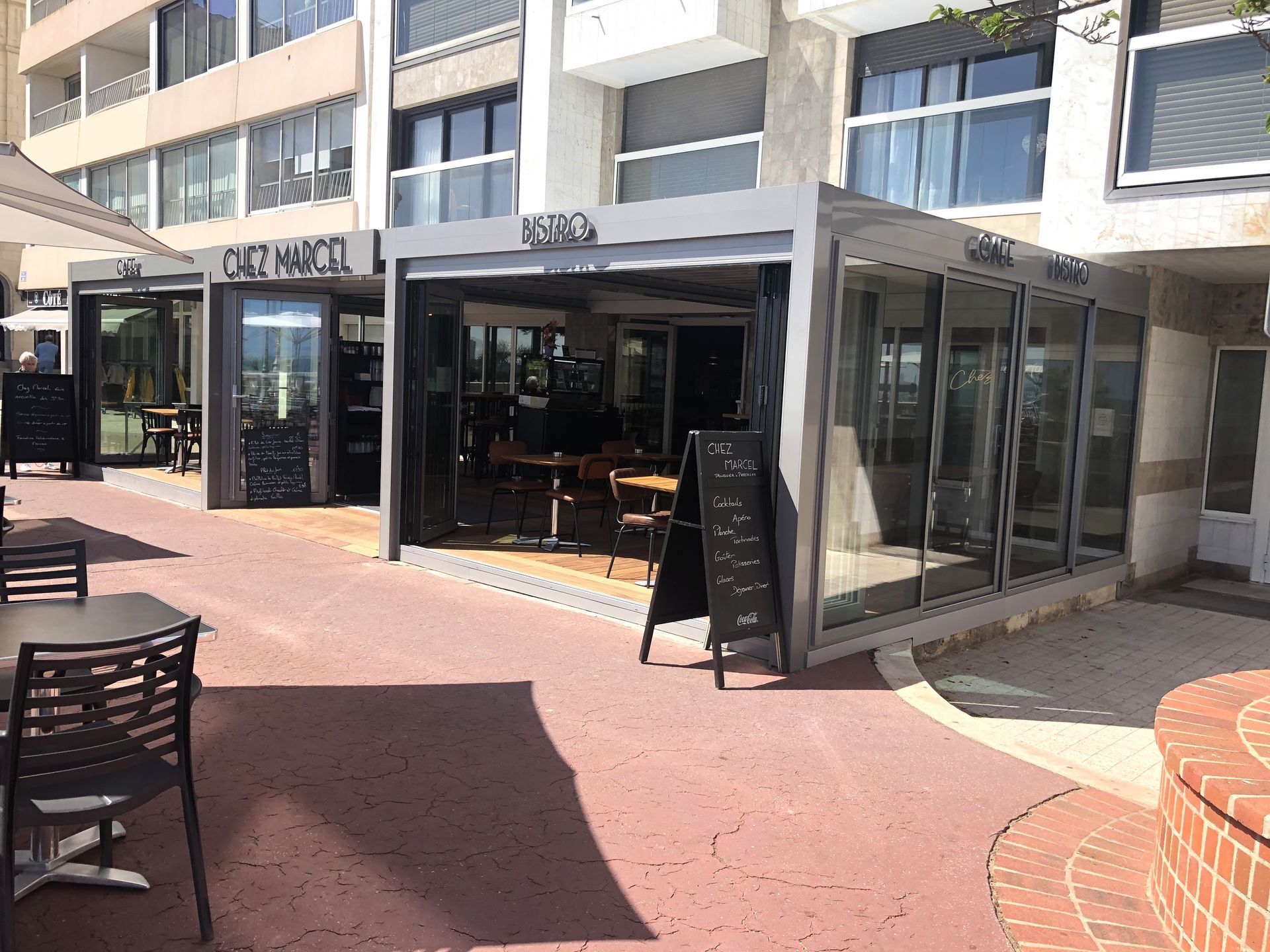 Terrasse de café à côté d'un bâtiment aux parois de verre sur une place ensoleillée
