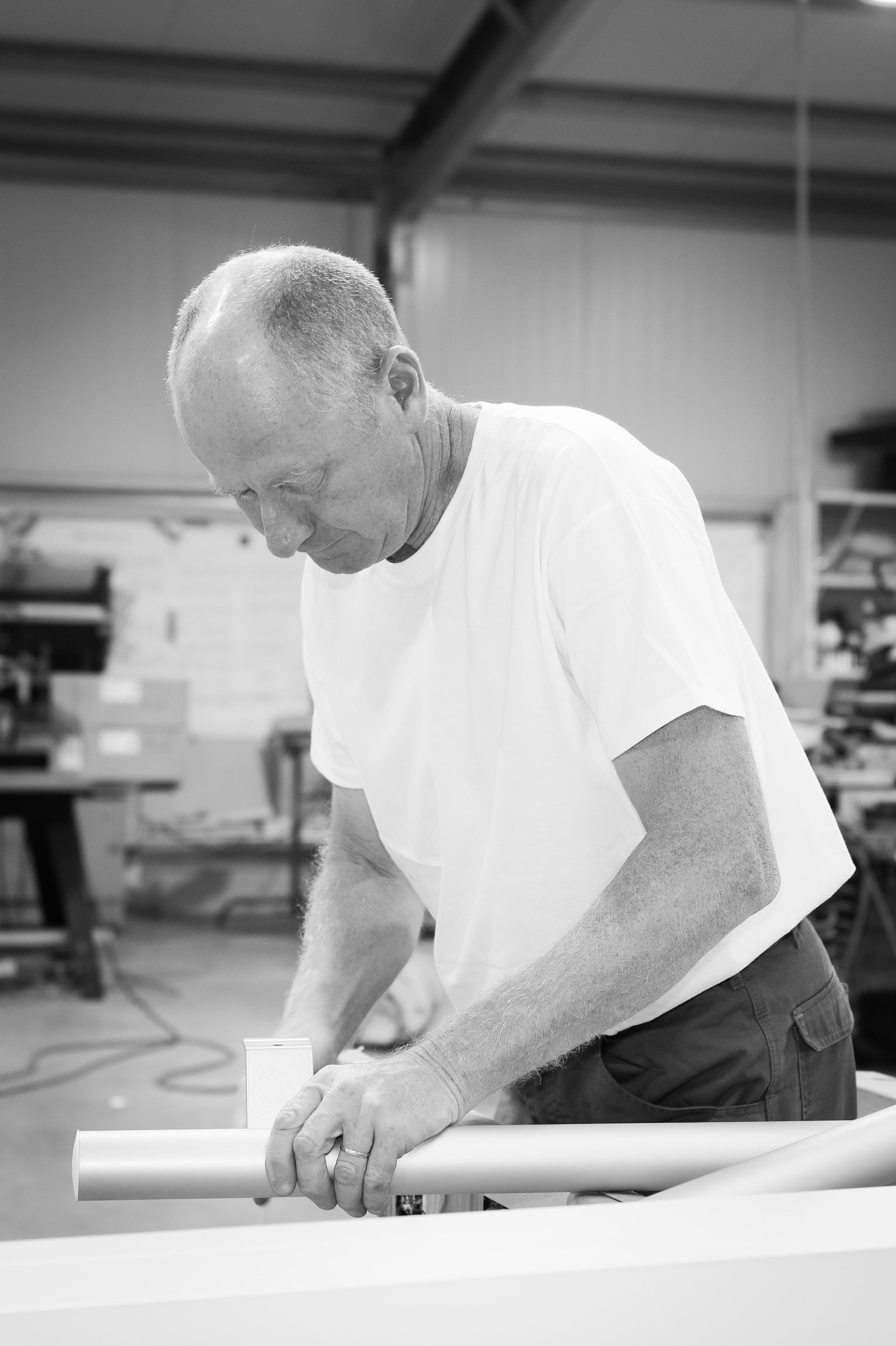 Une personne vêtue d'un t-shirt blanc se concentre sur l'assemblage d'un composant de tuyau métallique à un établi dans un atelier.