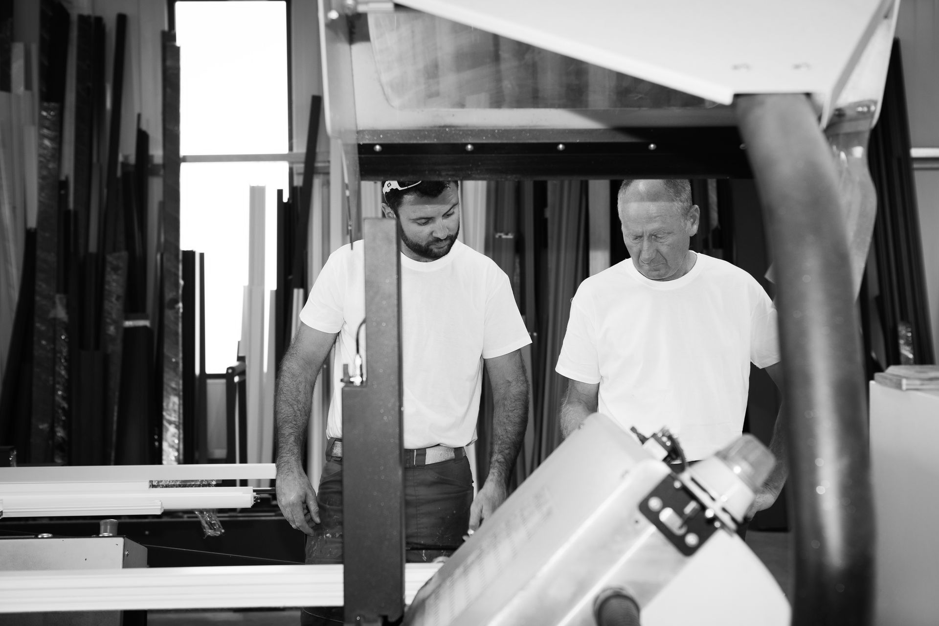 Deux personnes vêtues de t-shirts blancs travaillent ensemble à un poste de travail dans un atelier rempli de matériaux divers.