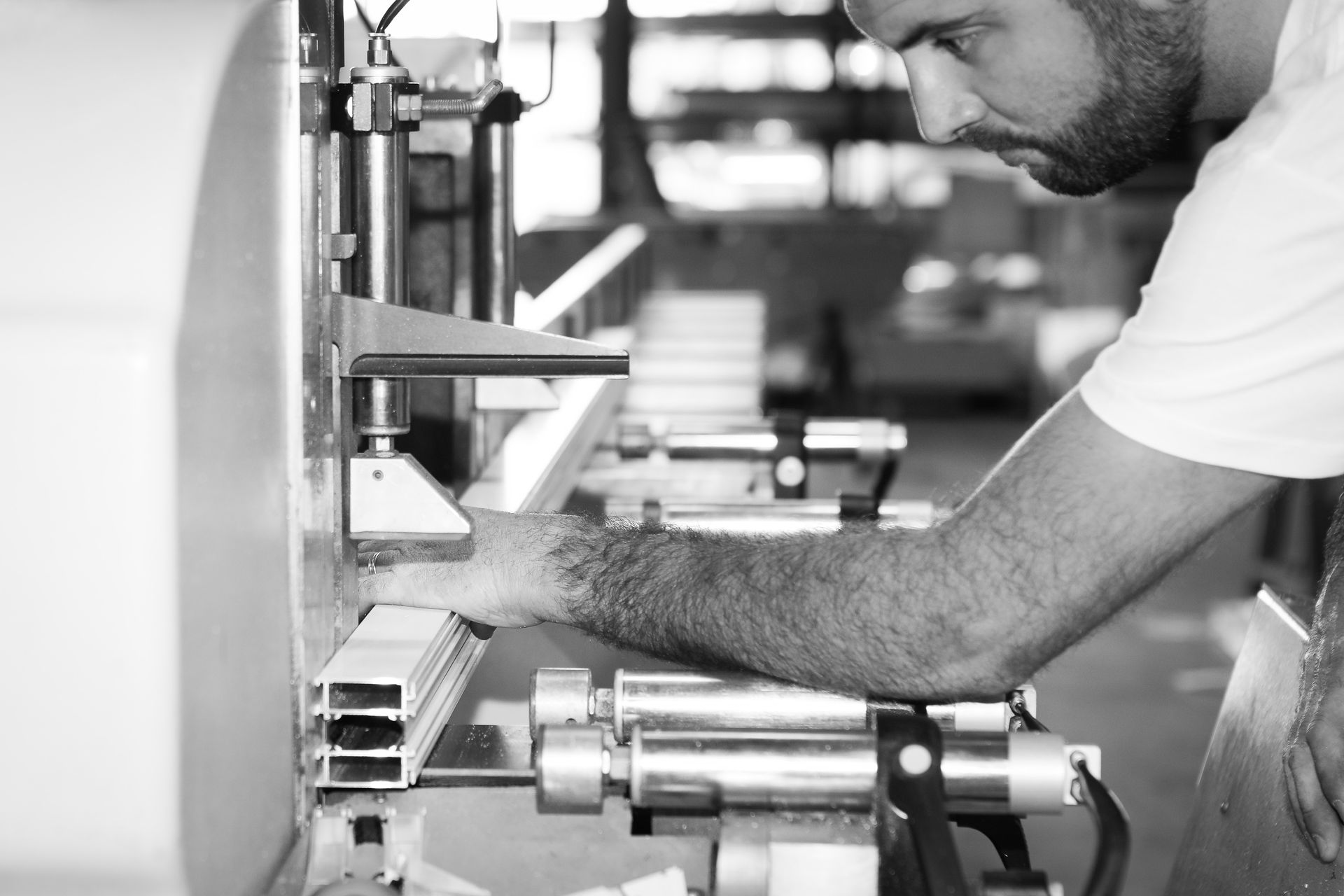 Un ouvrier actionne une machine dans une usine, ajustant manuellement un composant métallique sur une chaîne de production.