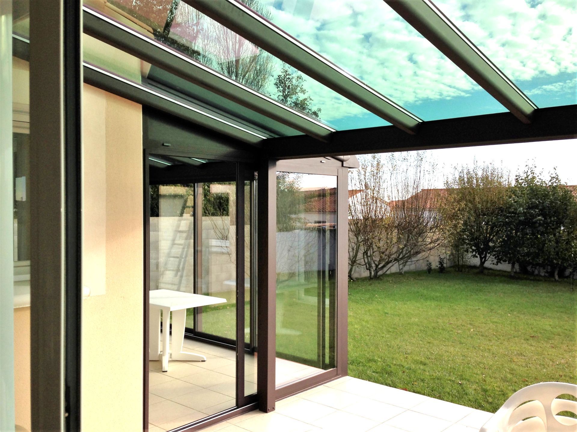Véranda avec portes vitrées ouvertes donnant sur un jardin verdoyant et mobilier de terrasse