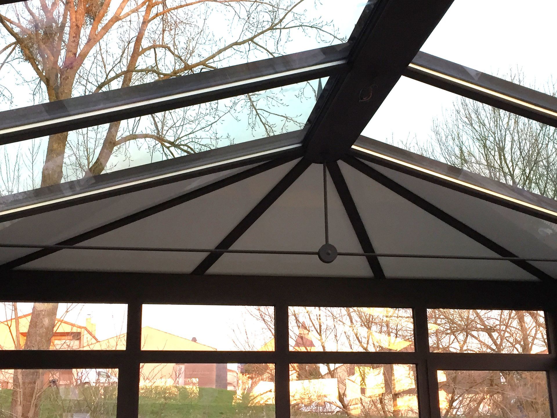 Pavillon à toit de verre et poutres sombres, vu d'en bas, se détachant sur les arbres et le ciel