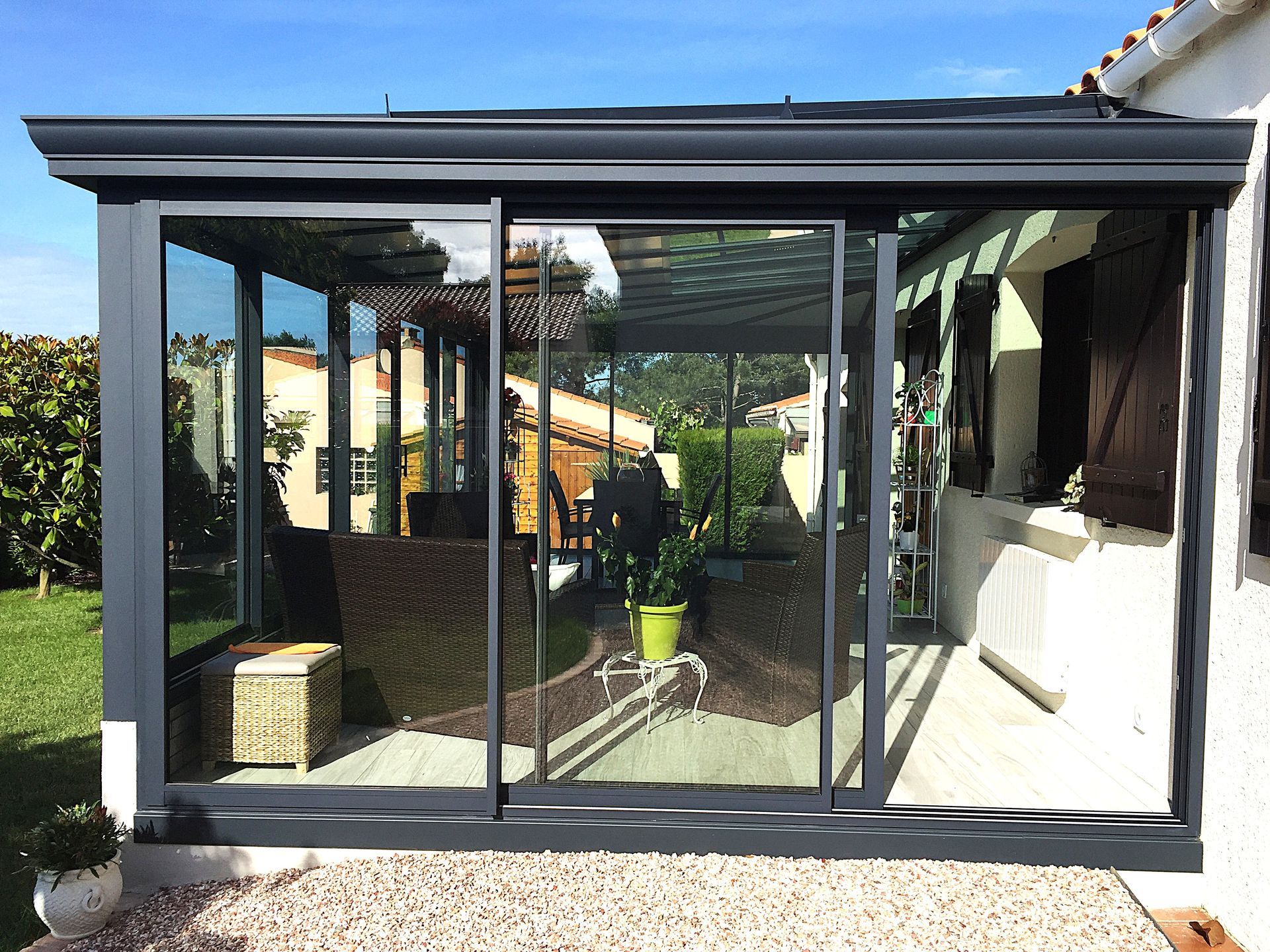 Patio vitré avec portes coulissantes, donnant sur un jardin et une pelouse