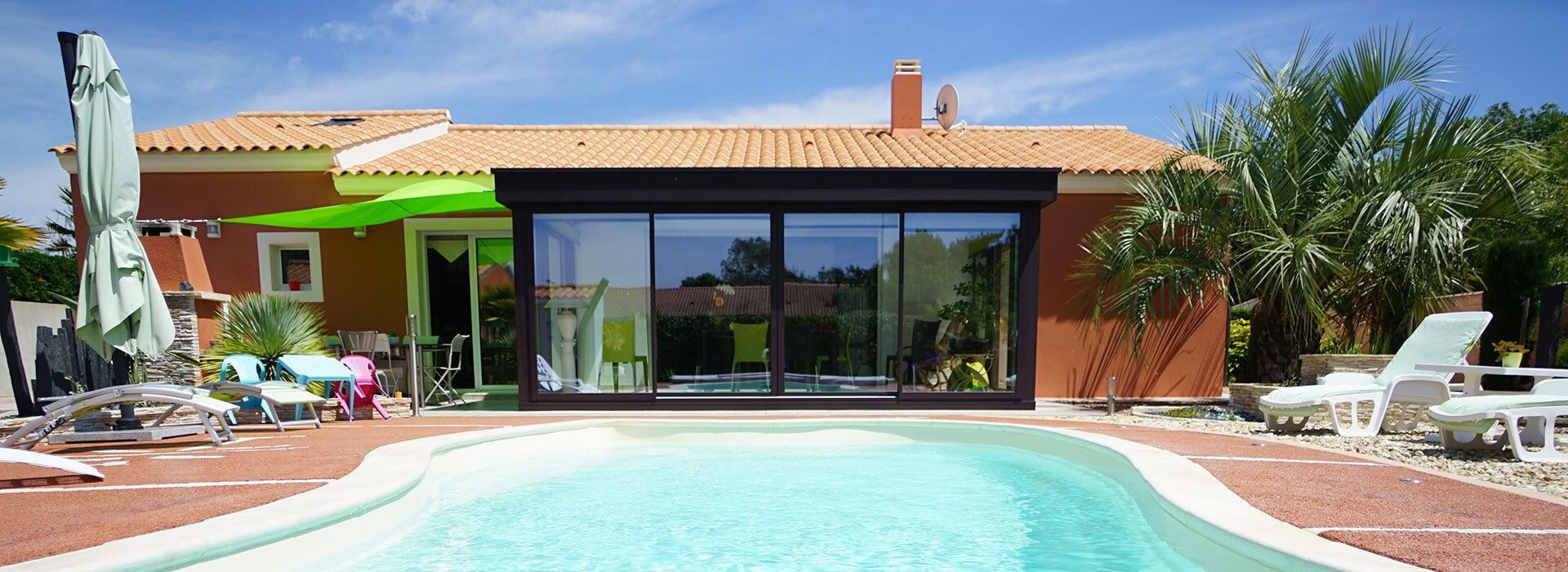 Jardin ensoleillé avec piscine turquoise, chaises longues sur la terrasse et maison moderne aux portes vitrées et au toit en tuiles