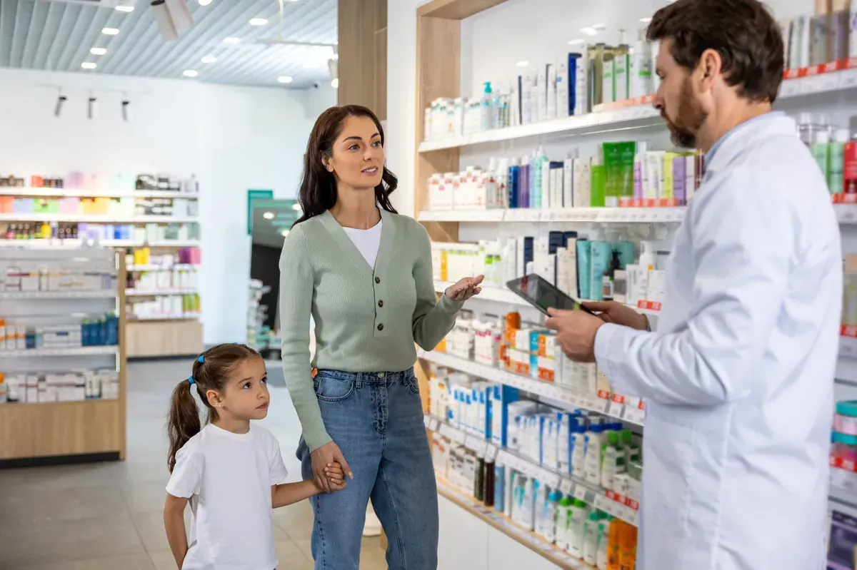 Una mujer y un niño consultan a un farmacéutico en una farmacia, discutiendo medicamentos cerca de los estantes de productos.