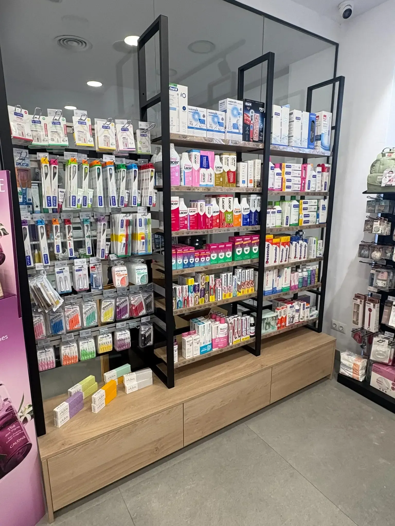 La mano de una persona alcanza una caja azul y blanca en un estante de una farmacia lleno de medicamentos.